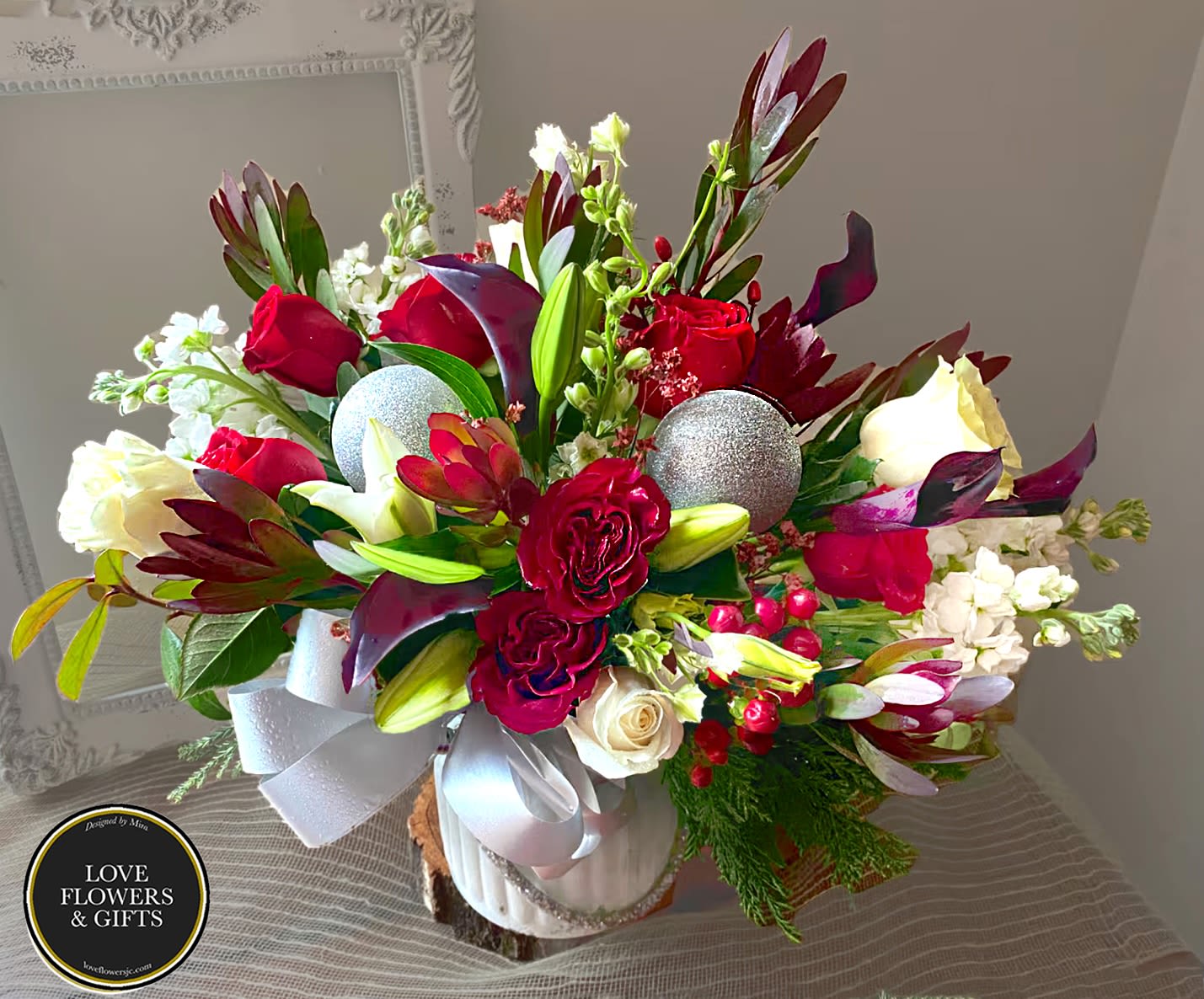 Burgundy &amp; Silver  - Designed in a frosted white vase made with fresh burgundy, reds, and whites with fresh seasonal greens with pops of silver for the a holiday vibe. 