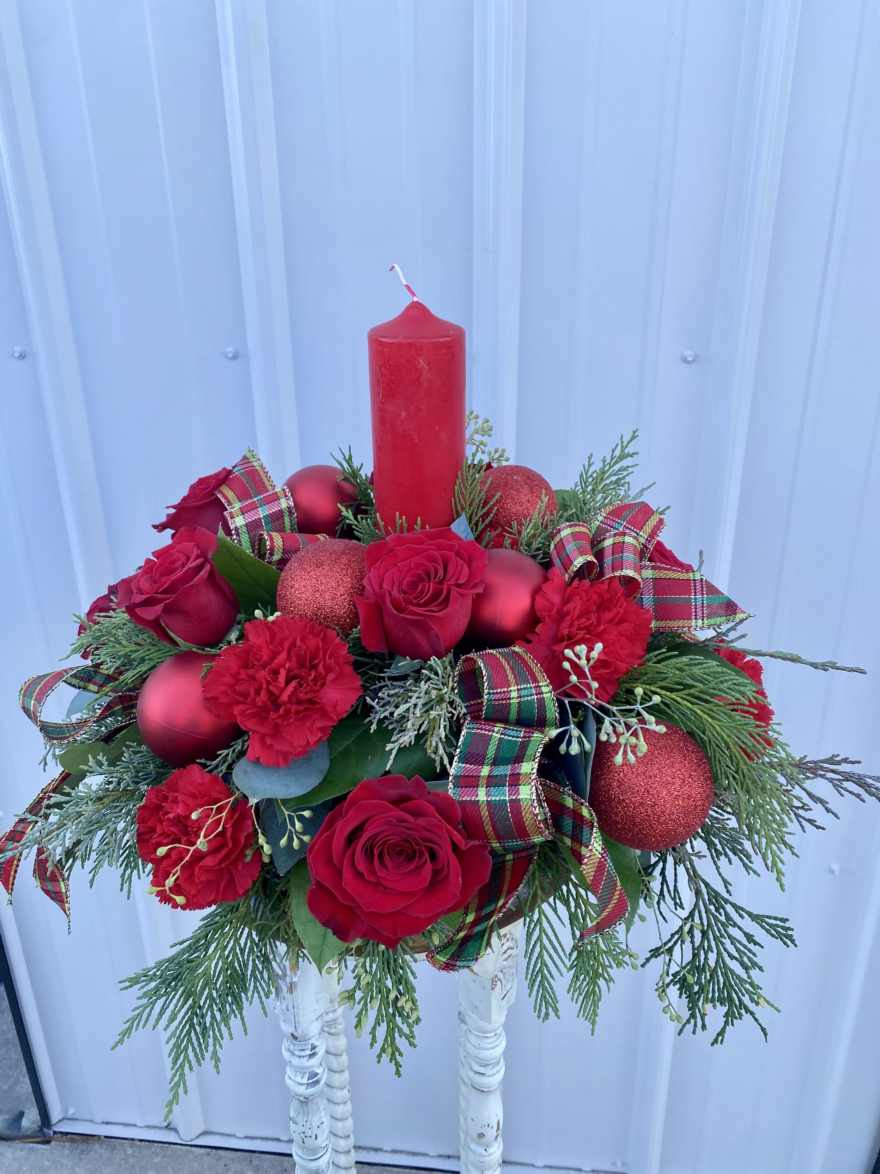 Holiday Harmony - Share peace and joy with everyone you love. Red Pillar candlelight tops the holiday's finest roses, daisies, carnations and winter greens. Adorned with ribbon, pinecones, and Christmas tree ornaments,