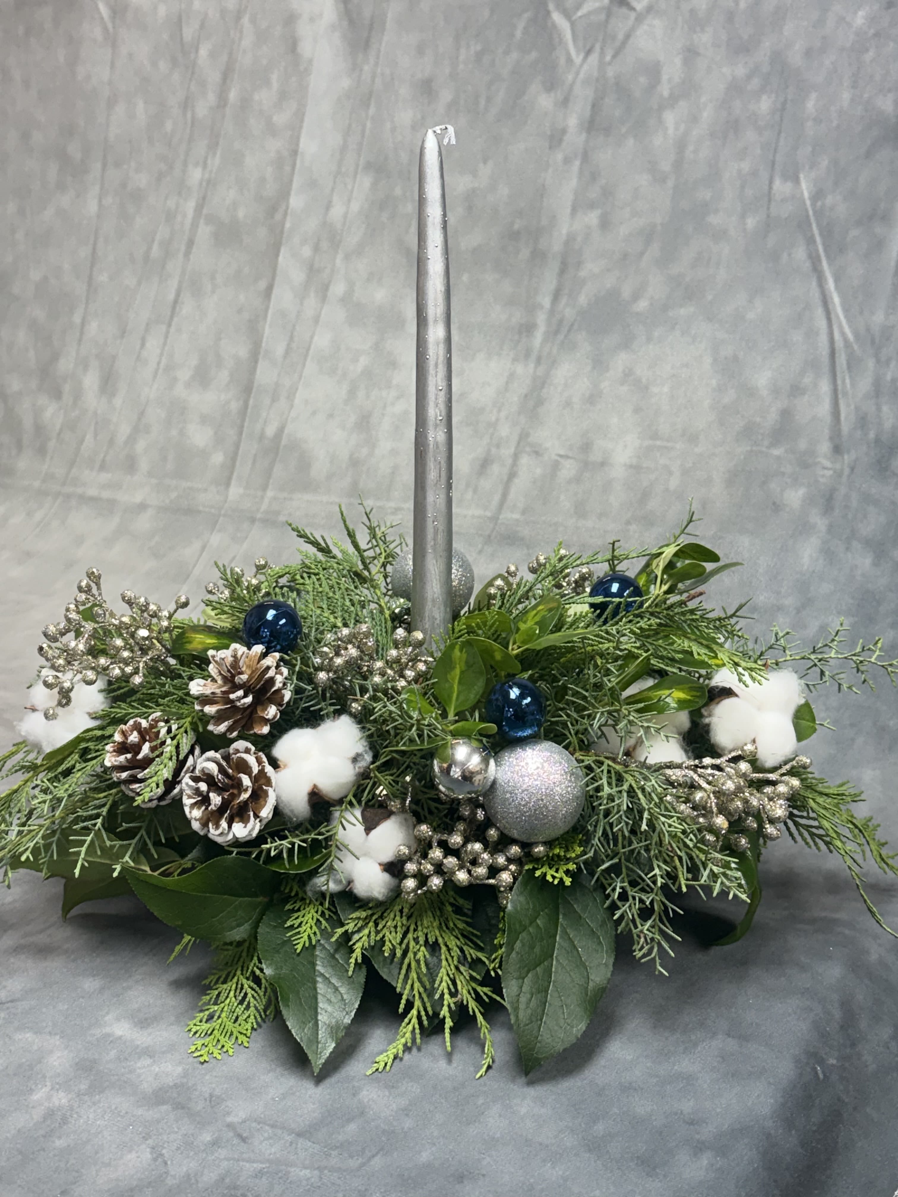 Sliver Blue Winter Glow  - Fresh greens, sparkling berries, icy pinecones, and soft cotton accents create a serene winter look topped with a shimmering silver candle.