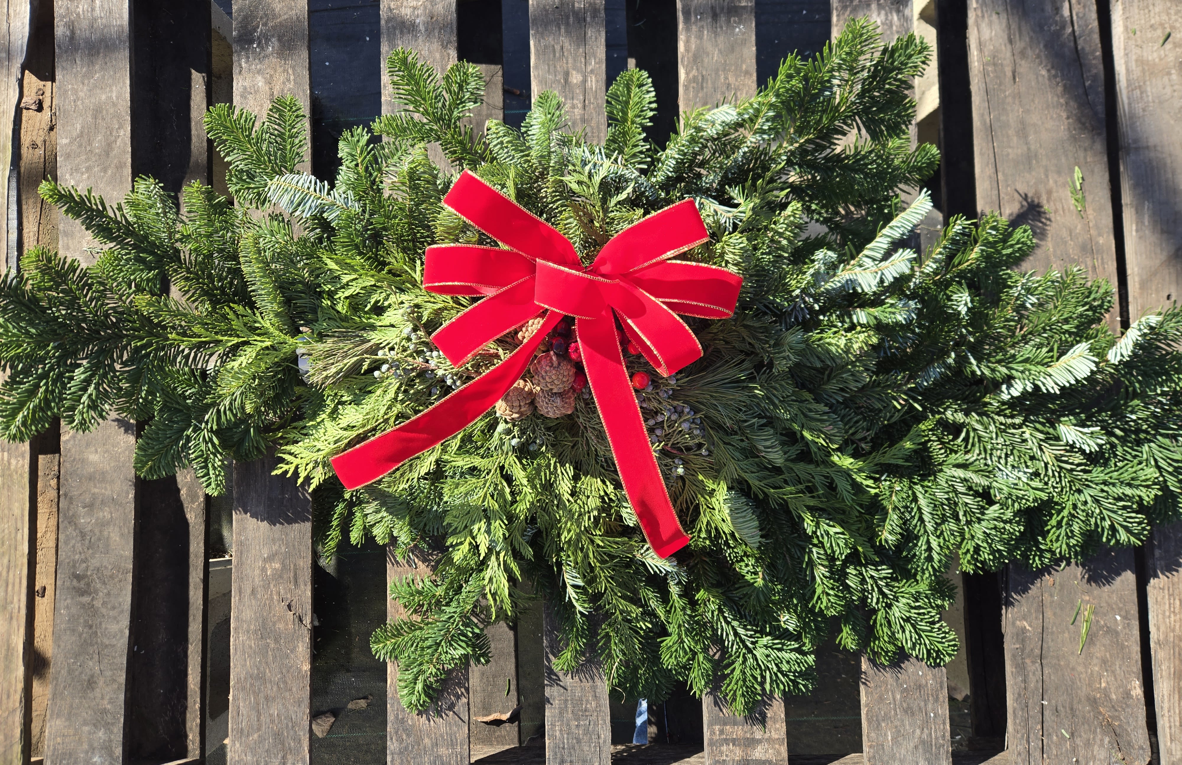 Hand Made Grave Pillows - Hand made holiday grave pillow—fresh greens, red berries, pine cones, and a red velvet bow. A beautiful tribute for the season. Available for pick up or delivery. *Cannot be delivered to cemetery gravesites*. Bow can be shifted for vertical or horizontal placement.  A beautiful way to honor your loved one.    Approximately 24" x 55"