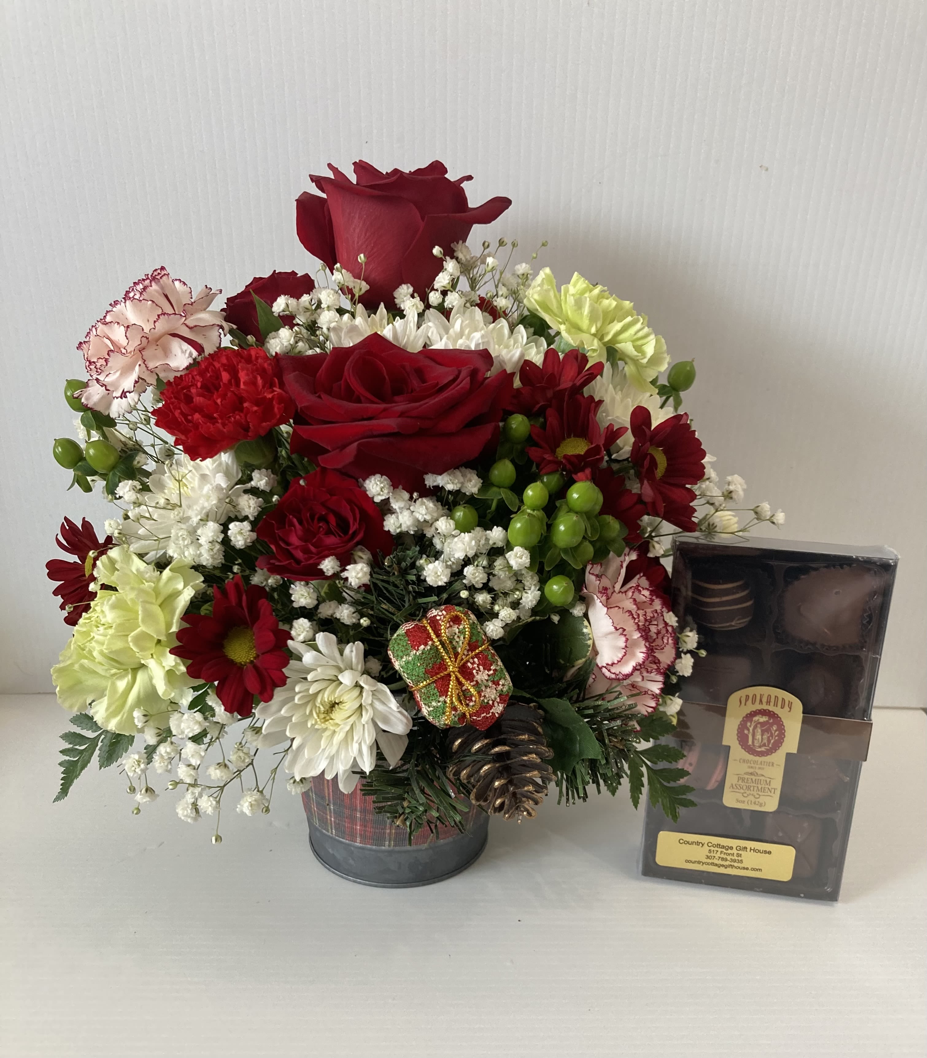 Christmas Celebration - Holiday arrangement in a cute plaid metal pot with Christmas tree on pot. Arrangement includes roses, peppermint carnations, spray roses, white carnations, mums, white daisy and greenery. Includes a box of delicious chocolates 