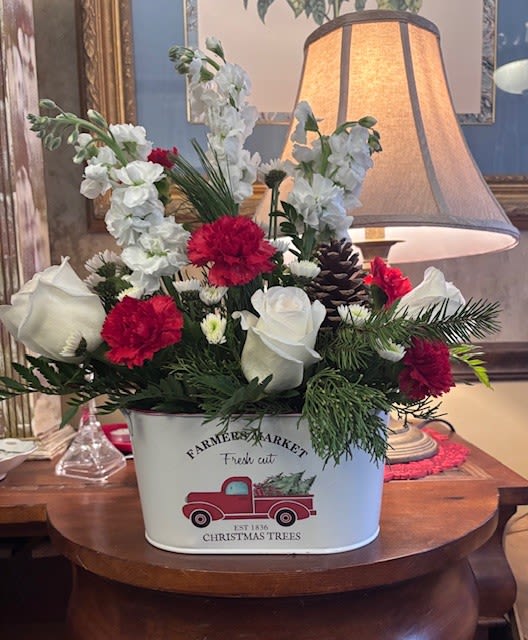 Country Christmas - What a special time of year and with this adorable keepsake tin filled with cheer, it's sure to make your holiday special. With white roses, red carnations, white cushion pomps and pine cone, this arrangement will bring joy for the whole season.