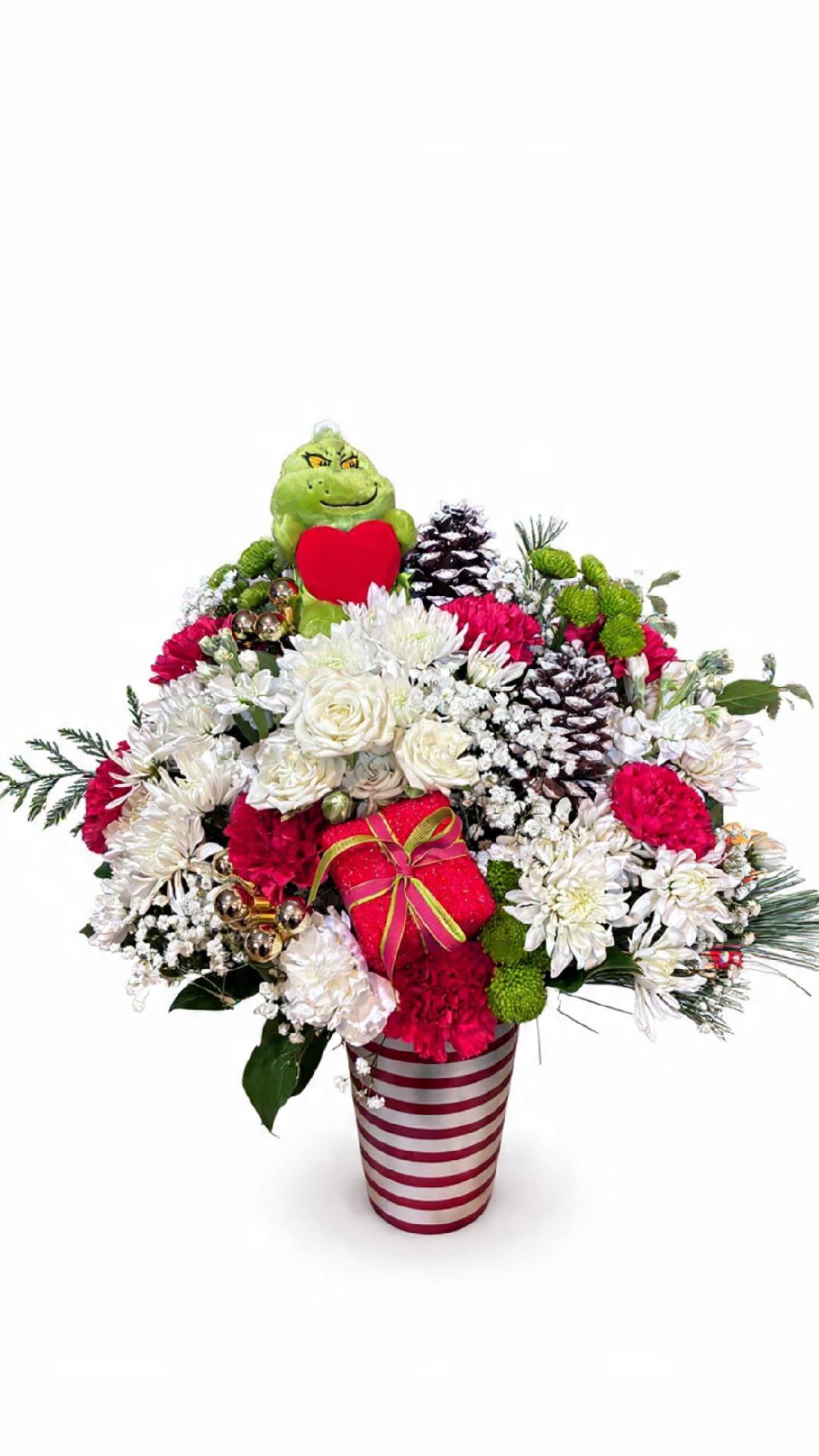 Grinchmas Candy Cane Bouquet - Bring some mischievous holiday cheer to your décor with this festive Grinch-themed arrangement! Featuring red and white blooms, frosted pinecones, playful ornaments, and a cute Grinch plush tucked inside, all presented in a candy-cane striped vase. Perfect for gifting or brightening up any Christmas space.