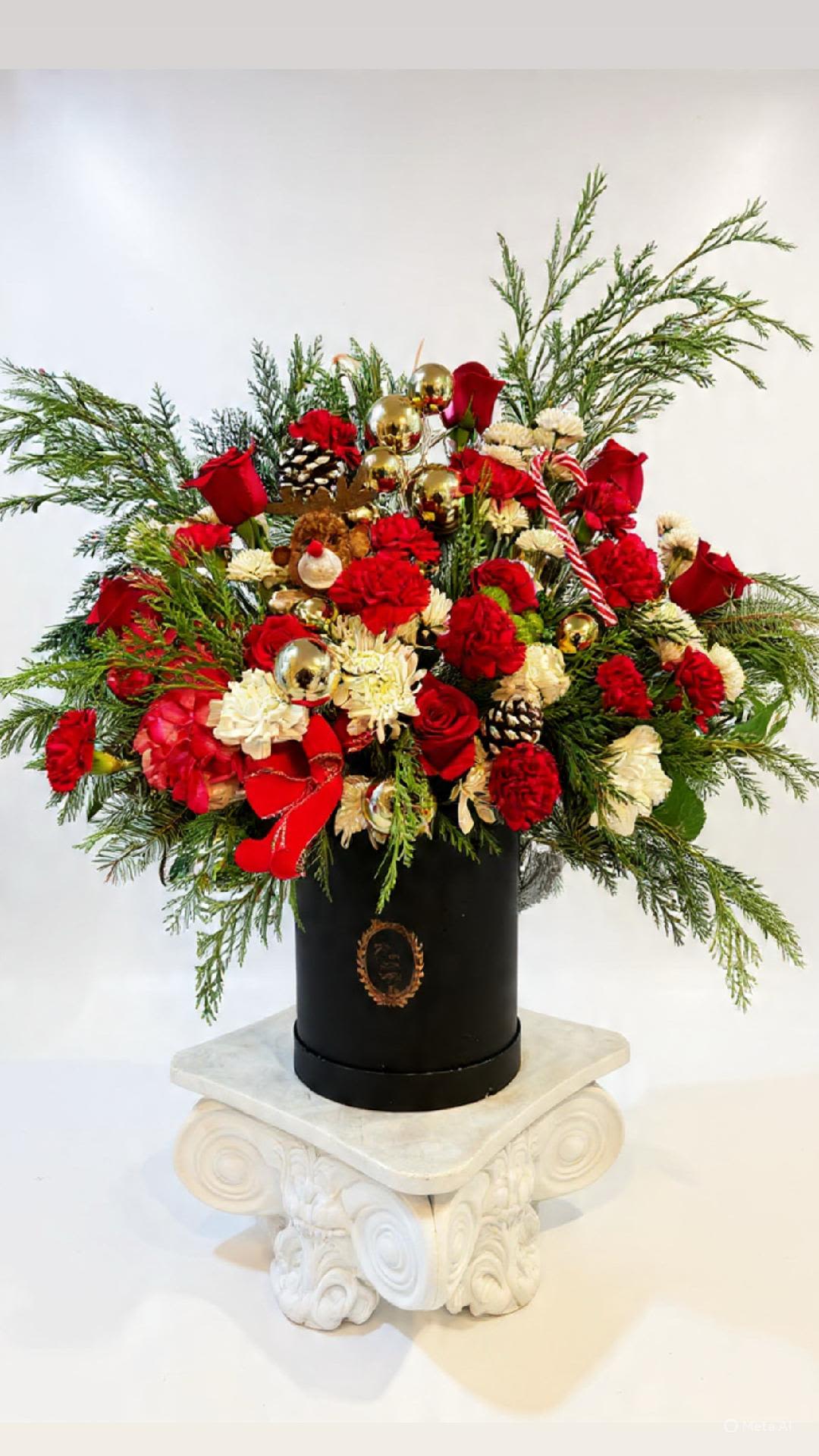 Grand Noël Designer Bouquet - An extravagant Christmas design showcasing premium red roses, carnations, seasonal greens, and winter accents finished with gold ornaments and ribbon details. Presented in a chic black hat box, this arrangement embodies luxury and holiday elegance.