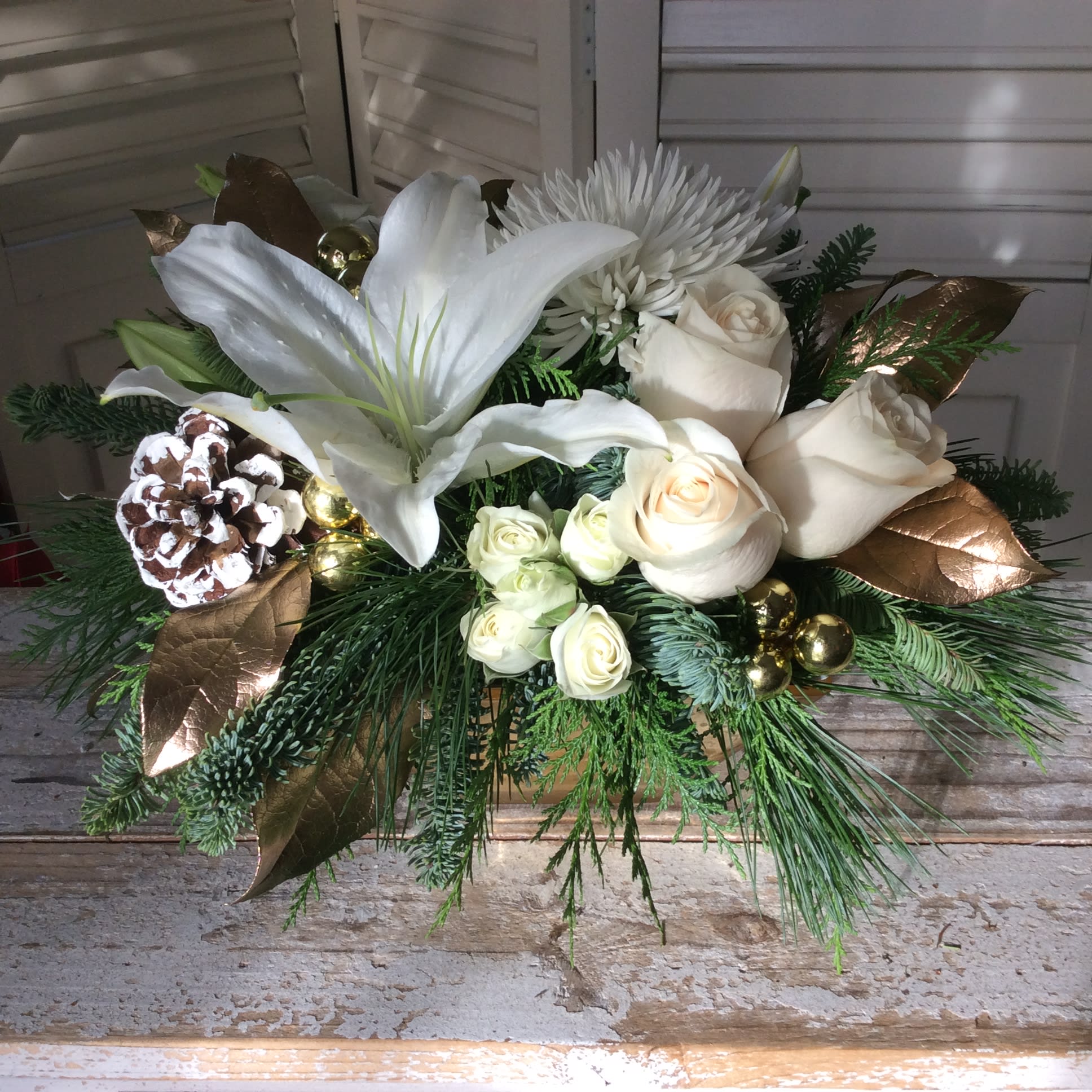 All that Glitters - Snow white flowers, including lilies, roses, and lisanthus, surrounded by sprigs of evergreen and gold leaves make this arrangement a classically beautiful choice for the holiday season.