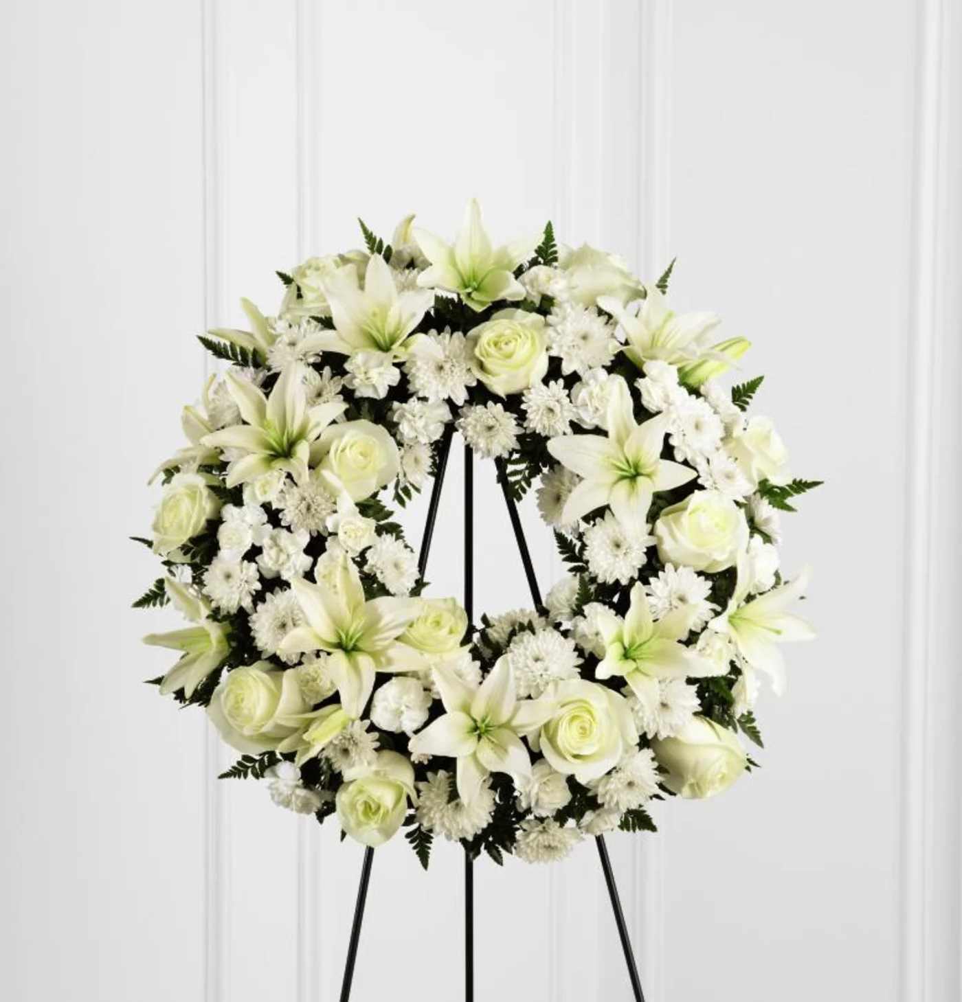 Treasured Tribute Wreath -  Treasured Tribute Wreath offers peaceful wishes of heartfelt sympathy with each delicate bloom. Bright white roses, Asiatic lilies, mini carnations and cushion poms are beautifully arranged to form an elegant accented with lush and vibrant greens. Displayed on a wire easel, this gorgeous tribute is a wonderful symbol of eternal life and sweet serenity. Approximately 20 inches in diameter. 