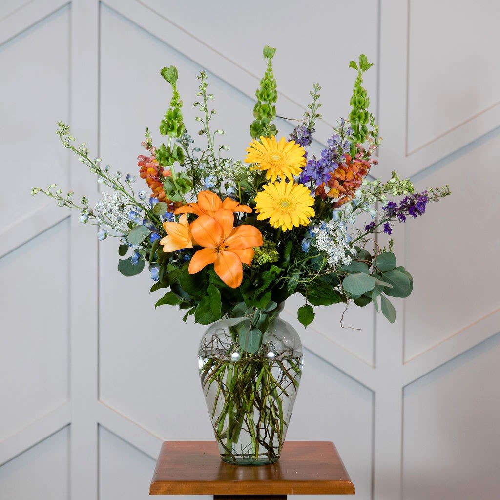 Barefoot - A bright, wildflower like arrangement with orange lilies, blue delphinium and yellow gerbera daisies, perfect to make a statement.  Approximate Size: 33&quot; H x 33&quot; W