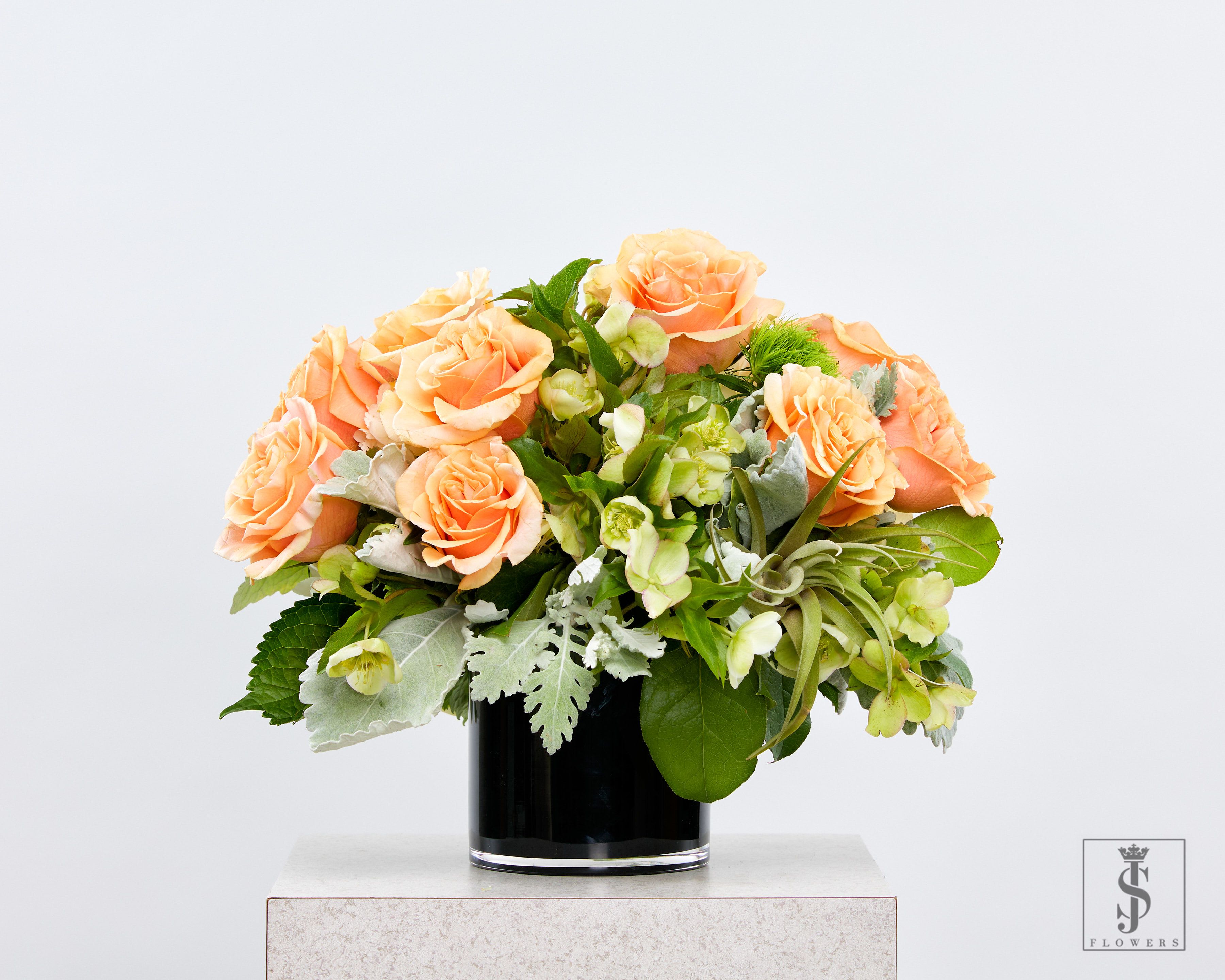 Amber Grace - Brighten any space with our luxurious peach rose flower arrangement, perfectly blended with seasonal greens and textures to create a timeless design. Featuring fresh peach garden roses, air plants, green hellebores, and dusty miller foliage, this handcrafted piece brings an elegant and refreshing charm to your home or event décor. Ideal for weddings, corporate gifting, birthdays, or simply adding a touch of beauty to your living space.  Expertly arranged in a sleek black glass vase, this floral design radiates sophistication and warmth. Now delivering across DFW metro areas – elevate your floral experience with this unforgettable botanical masterpiece.