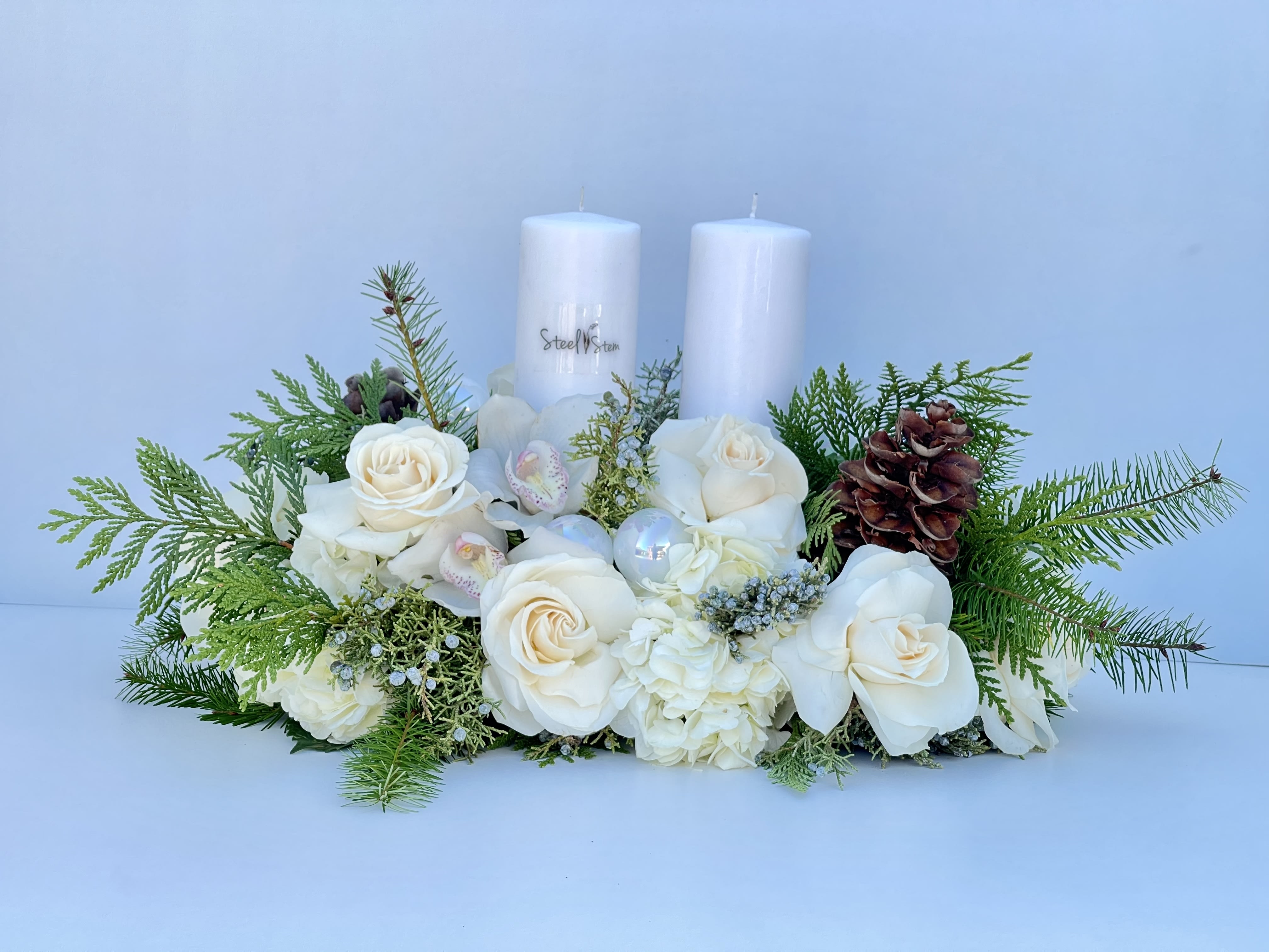 Winter Day - Winter centerpiece arrangement with mix pine greens, pine cones, white rose, white cymbidium orchids, white hydrangea, white ornaments and two candles.  A perfect statement piece for your home or an exquisite gift that can be enjoyed in this Special holidays.