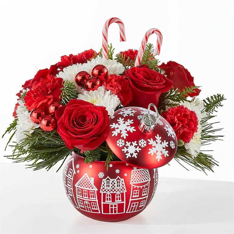 Cheer In the Air Ornament - Send a gift that embodies holiday magic and joy. This festive arrangement brims with vibrant red roses, cheerful red carnations, and soft white poms, complemented by seasonal greenery and bright red ornament accents. Two classic candy canes add a whimsical touch, making this bouquet perfect for spreading holiday cheer. Cheer in the Air Ornament  is approximately 12"H x 13"W.