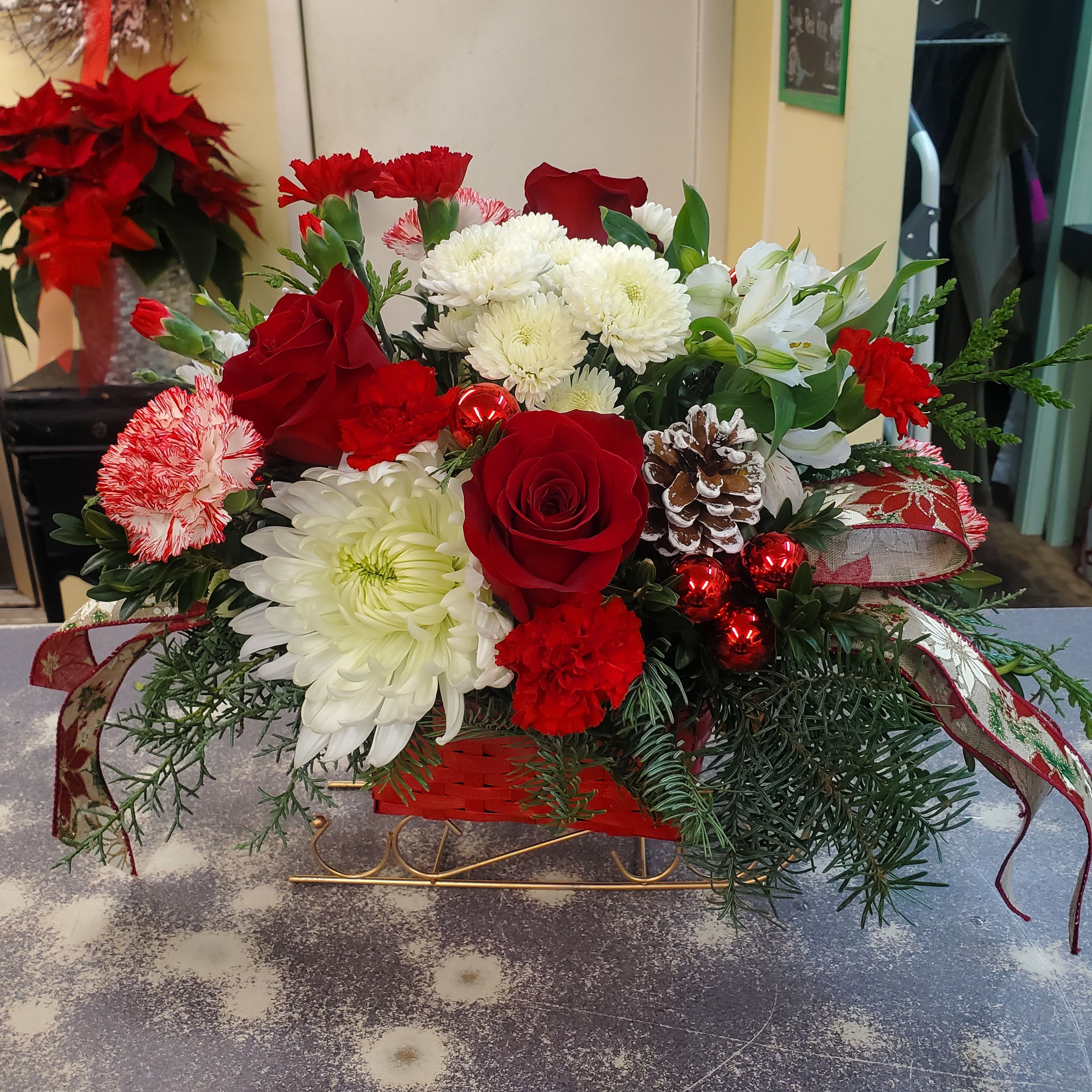 Sleigh Ride - A wicker sleigh filled with assorted winter greens,  flowers and accented with pine cones, ribbons and balls.  