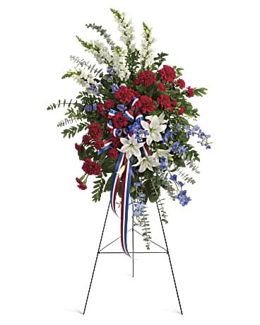 American Flag Spray  - Sparkling like an Independence Day fireworks display, a striking red, white and blue spray stands tall proud and patriotic. Bearing the colors of our nation's flag, it's a grand and fitting tribute to members of the military and American heroes. Adorned with yards of multicolored patriotic ribbon, this easel-mounted standing spray features flowers such as red carnations, white asiatic lilies and snapdragons, and blue delphinium, along with an assortment of greens.