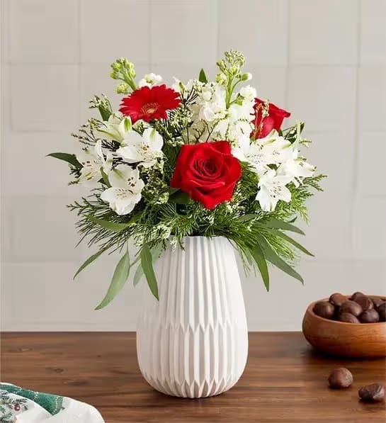 Dazzling Christmas™ Bouquet - Celebrate the most magical time of year with our dazzling bouquet. A rich gathering of blooms in classic red and white is accented by lush greenery. Hand-designed in our keepsake White Modern Vase, featuring a tapered design and matte finish, it’s a gift that brings the joy of Christmas to family and friends, near and far.  All-around arrangement with red roses and mini Gerbera daisies, white stock, Peruvian lilies (alstroemeria) and Limonium; accented with feather willow eucalyptus and assorted Christmas greenery Artistically designed in our Modern White Vase, with a tapered design and a matte finish, for a contemporary look that also has a softness to it, to complement everyday arrangements; measures 8"H x 5.35"L x 5.35"W Premium arrangement measures approximately 20"H x 16"W  Deluxe arrangement measures approximately 19"H x 15"W  Standard arrangement measures approximately 18"H x 14"W  Our florists hand-design each arrangement, so colors and varieties may vary due to local availability To ensure lasting beauty, Peruvian lilies may arrive in bud form and will fully bloom over the next few days