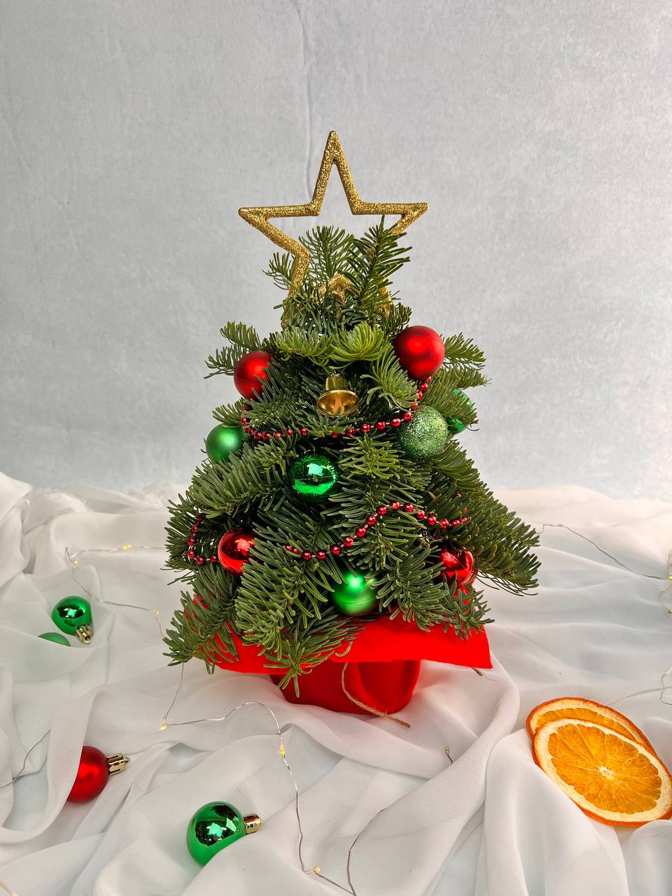 Jolly Tree - A festive mini Christmas tree designed with fresh evergreens, red and green ornaments, and a sparkling gold star topper. This compact holiday arrangement brings classic Christmas charm to any home or office. A perfect gift for the season and available for delivery in West Hollywood and Beverly Hills from The Purple Rose.