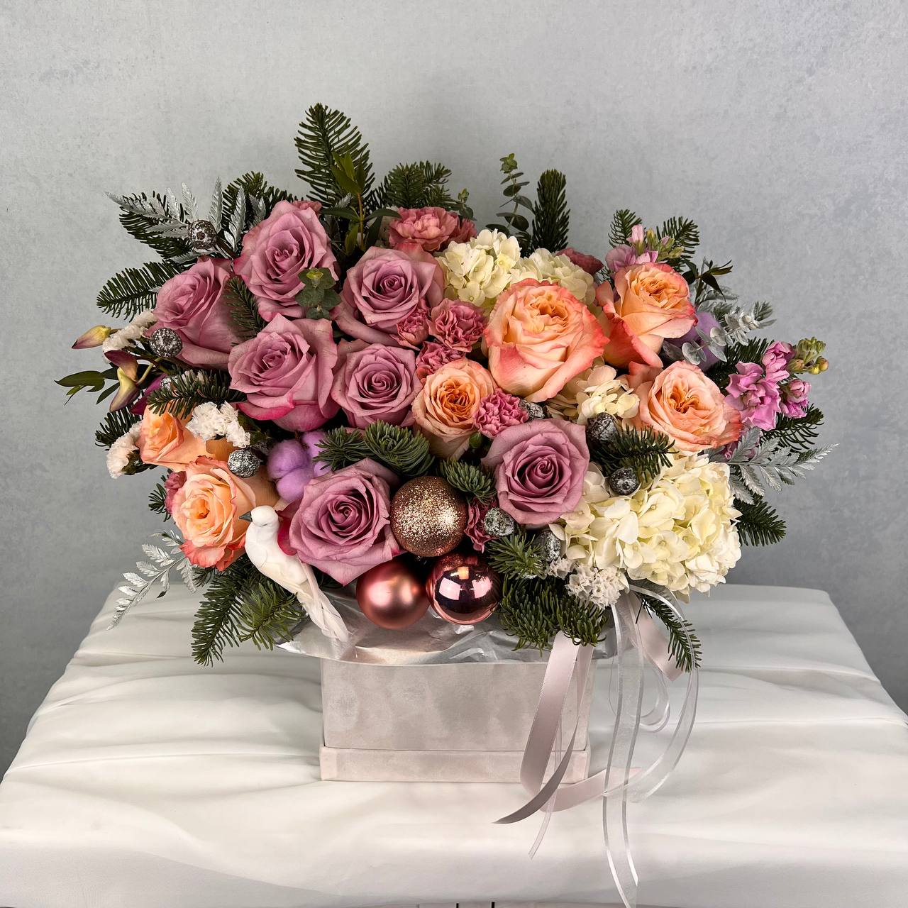 Anastasia - A luxury winter arrangement designed with mauve roses, peach garden roses, spray roses, hydrangea, and seasonal evergreens. Accented with soft metallic ornaments for a festive touch, this piece brings an elegant winter feel to any home or celebration. A perfect gift for the holidays, winter birthdays, and special occasions.Hand delivered across West Hollywood, Beverly Hills, and nearby areas. STANDARD size is shown in the main picture.  