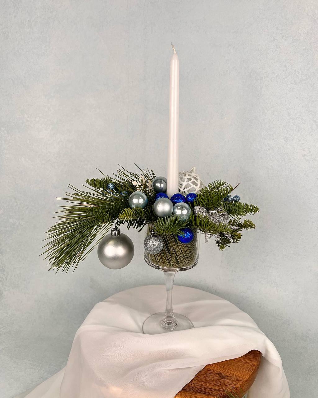 Winter Candlelight - A refined winter centerpiece crafted with holiday evergreens, blue and silver ornaments, and a tall taper candle for a clean, elegant look. Perfect for Christmas parties, dining tables, and winter home decor.