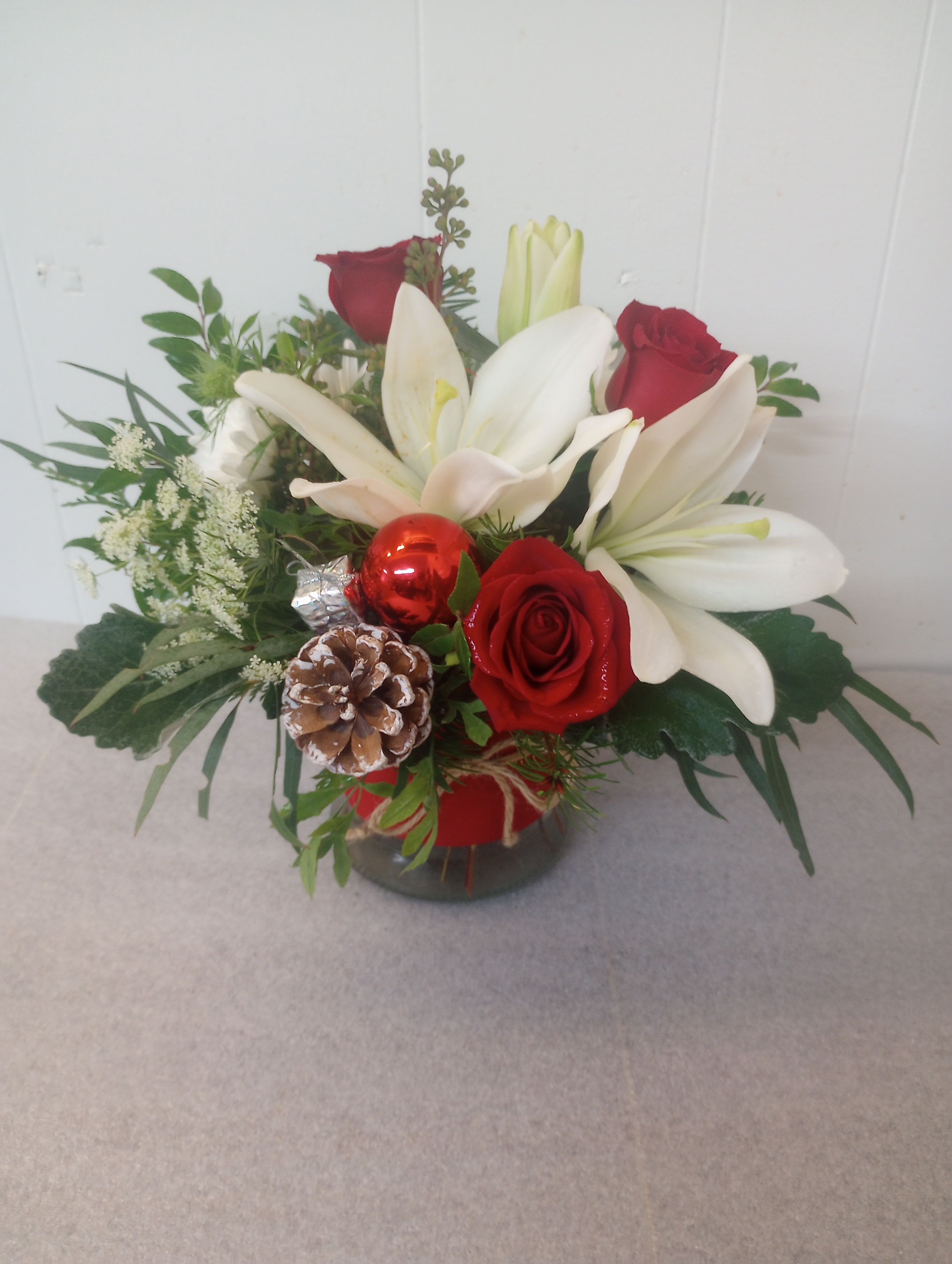 Time of Year - White Asian lilies and rd roses tucked together with Christmas greens in a low glass container. 