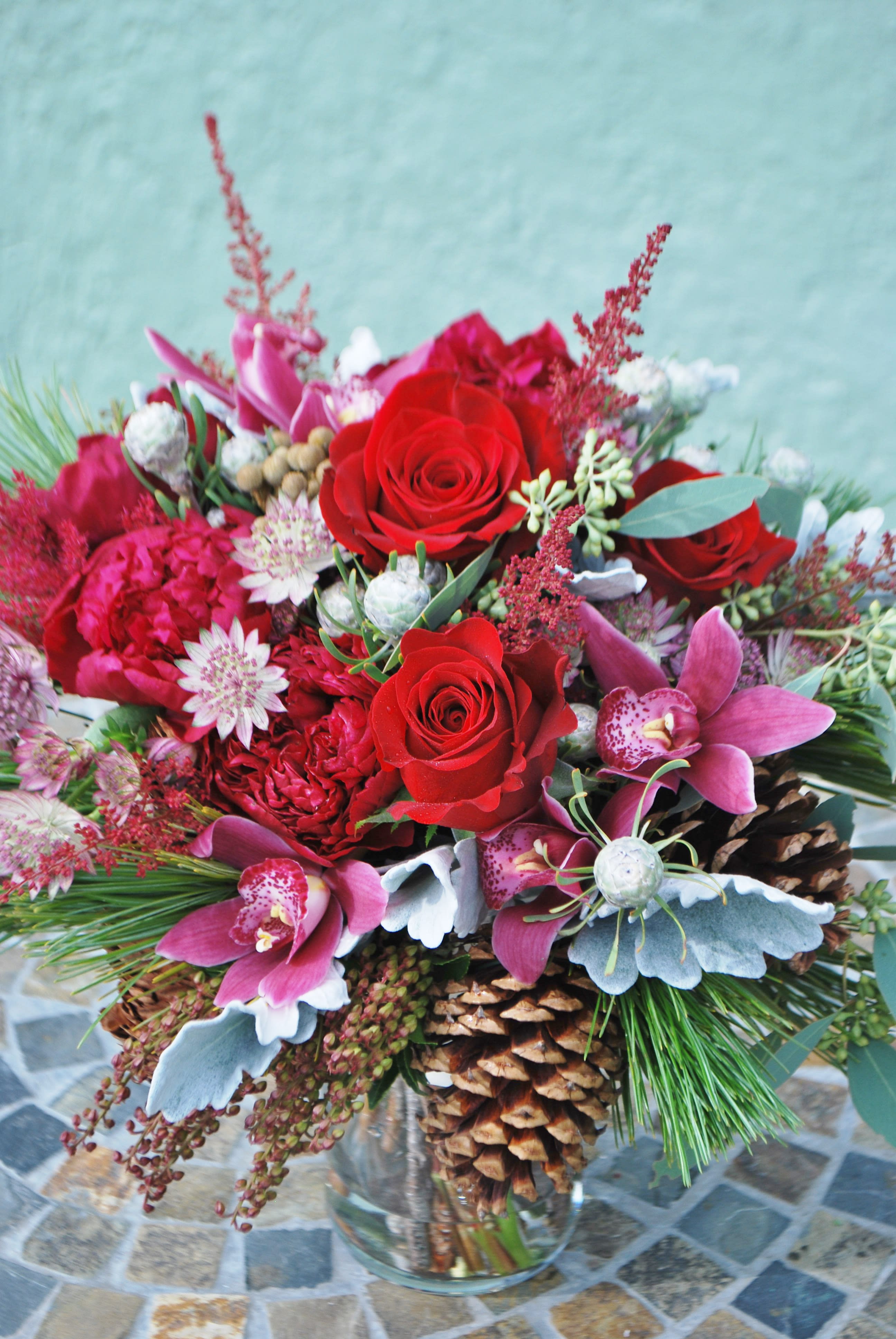 Winter Solstice - Winter blooms beautifully in this design featuring red roses, cymbidium orchids. Arranged with wintery evergreens and dusty miller, it is red but very serene and calm as well. . 