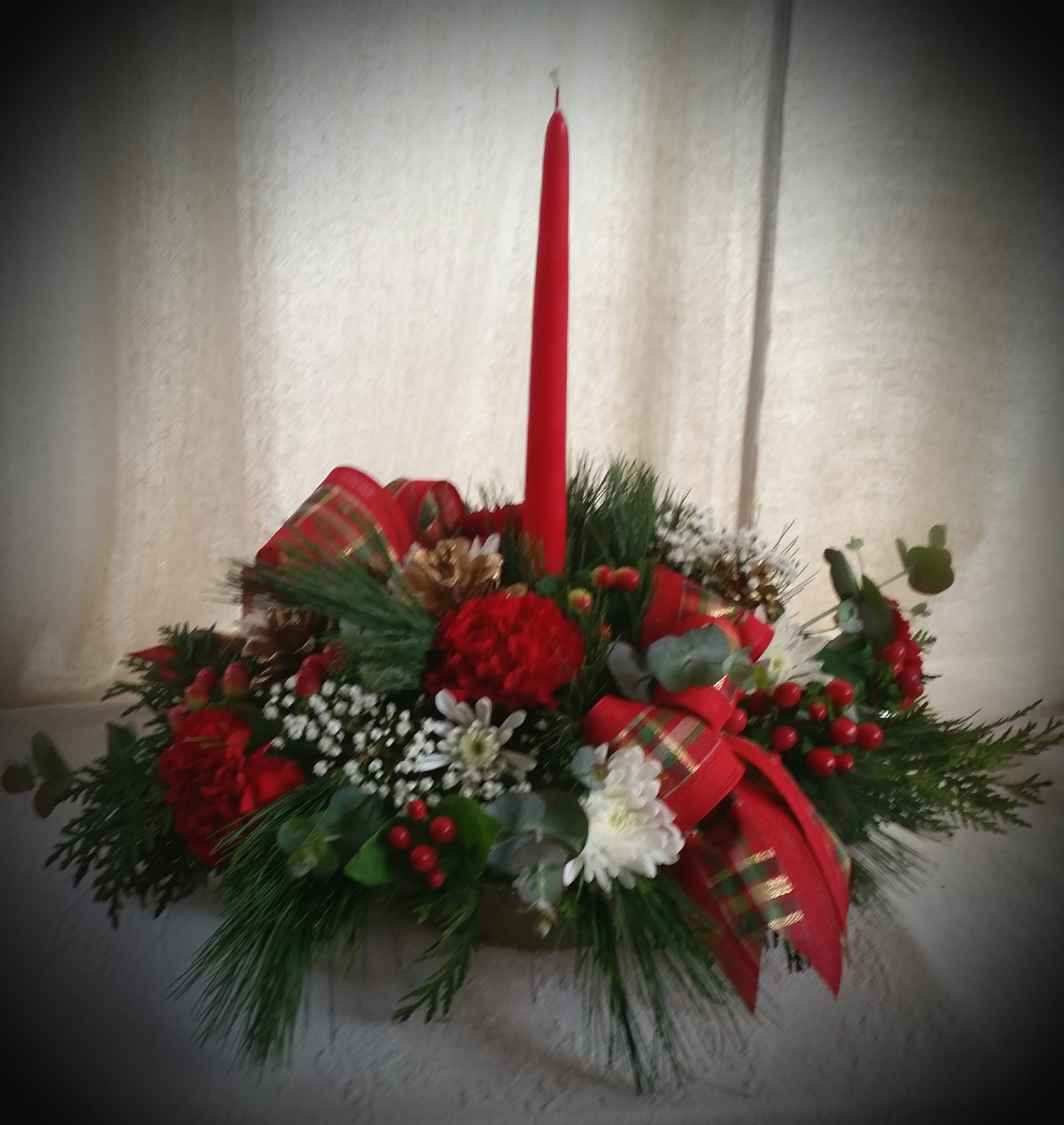 Holiday Centerpiece - This oblong centerpiece is made of fresh locally-grown greens, chrysanthemums, hypericum, carnations and baby's breath.  It's embellished with ribbons, a candle and pine cones.