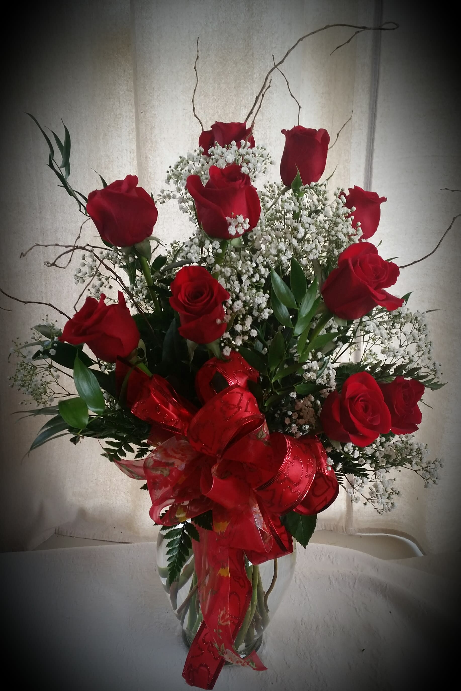 One dozen red roses - A dozen red roses arranged in a vase with fern and baby's breath.  The deluxe version includes a variety of greens and fillers.