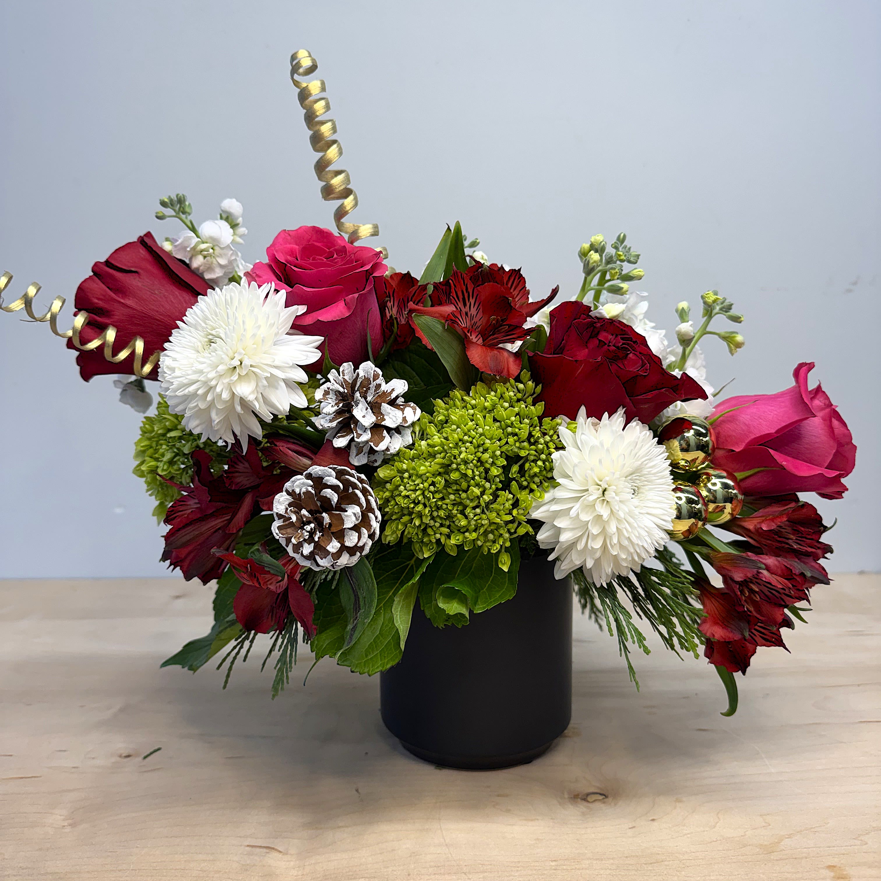 The Christmas Surprise - The name says it all!  The perfect gift for a hostess or friend this holiday season.  This petit arrangement comes in a black porcelain container, and shines with a mix of Roses, Alstromeria, Mini Green Hydrangea, and pops of golden accents.  Finished, this arrangement ranges 10-14"