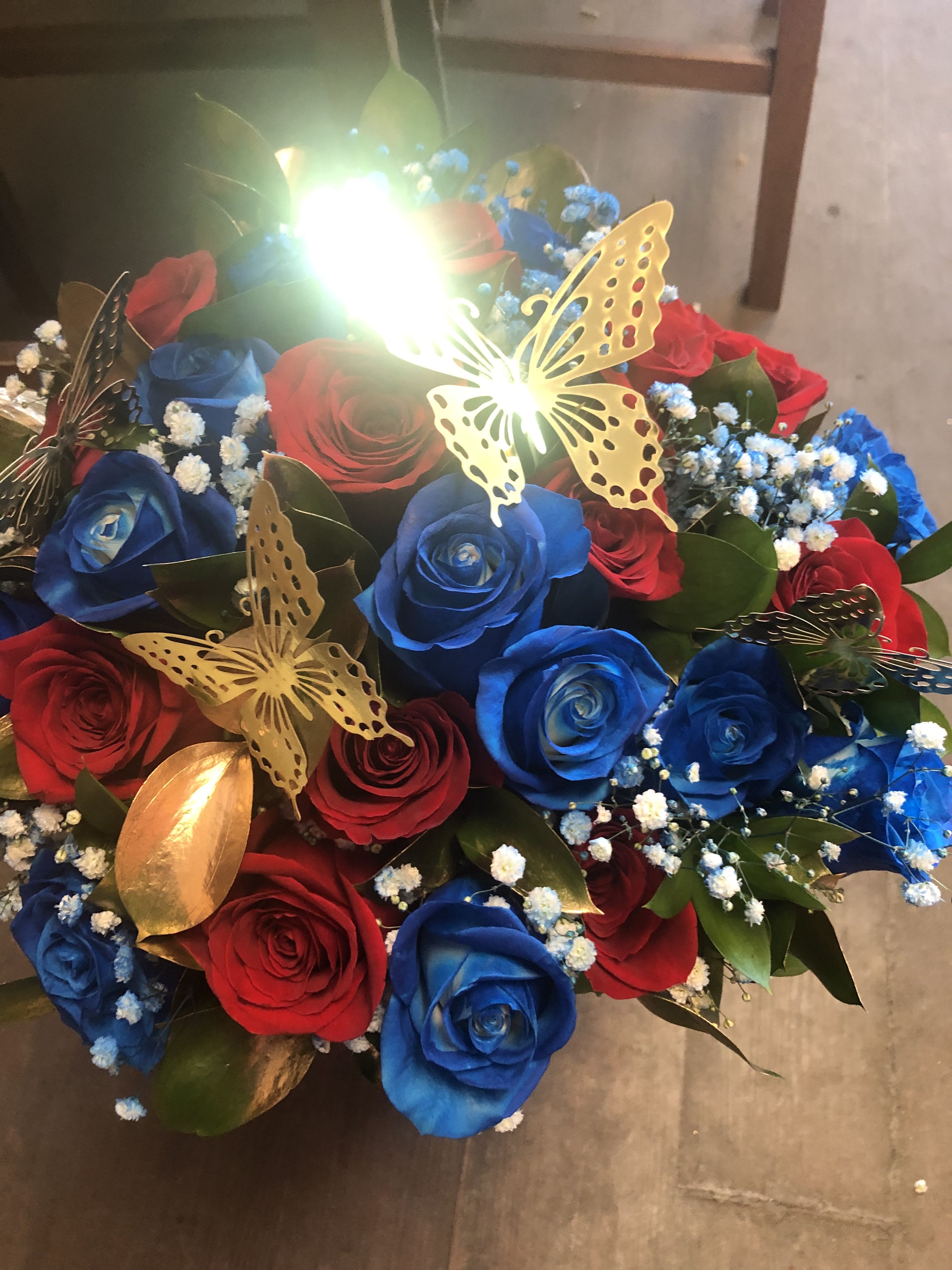 RED AND BLUE ROSE WRAP (24 ROSES) - 12 RED ROSES AND 12 BLUE ROSES (NOTE THE BLUE ROSES ARE SPRAY PAINTED THIS COLOR) IN A WRAP WITH GOLD RUSCUS LEAVES AND BABY BREATH ALSO SPRAY PAINTED BLUE AND GOLD BUTTERFLIES.  WRAPPED IN BLACK KOREAN PAPER.   DELUXE PRICE INCLUDES 36 ROSES PREMIUM PRICE INCLUDES 48 ROSES 