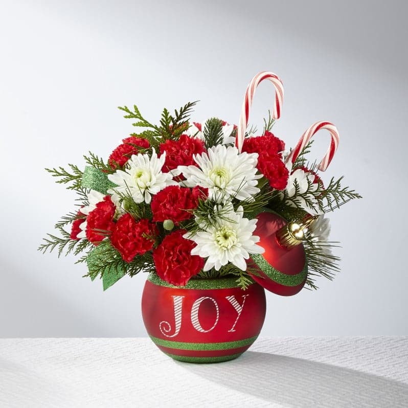 The FTD® Season's Greetings™ Bouquet: 17-C5s - The FTD® Season's Greetings™ Bouquet is ready to dazzle your special recipient this holiday season! Rich red roses, red mini carnations, white carnations, and white chrysanthemums, accented with fragrant holiday greens are arranged by our floral artisans to create a very merry Christmas bouquet. Presented in a keepsake sparkling red ceramic ornament inspired vase, accented with green stripes and the word, "Joy," on the front in white, with a matching lid to create a treasured Christmas accent piece, this holiday bouquet is also embellished with two peppermint candy canes to create a truly remarkable Christmas gift.