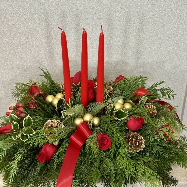 Christmas Centerpiece - Create a warm and festive atmosphere this holiday season with our classic Christmas centerpiece. Designed with traditional holiday charm, this arrangement features lush evergreens, red roses, pinecones, holly and accents of golden ornaments all beautifully complemented by three elegant red taper candles.