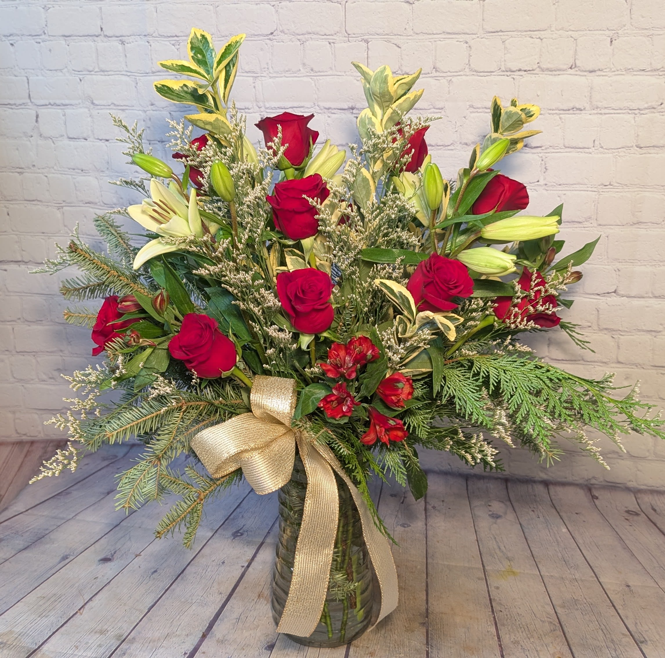 Yuletide Glow - Radiate holiday elegance with Yuletide Glow, a luxurious vase arrangement designed to make a statement. This stunning piece features a dozen premium red roses paired with graceful white lilies, creating a classic and timeless Christmas palette. Lush seasonal greens—Port Orford cedar, Fraser pine, and euonymus—add texture, fullness, and that unmistakable evergreen fragrance. Soft touches of white limonium complete the look with a delicate wintery finish. Perfect for gifting or elevating your own holiday décor, Yuletide Glow brings warmth, beauty, and festive sophistication to any space.