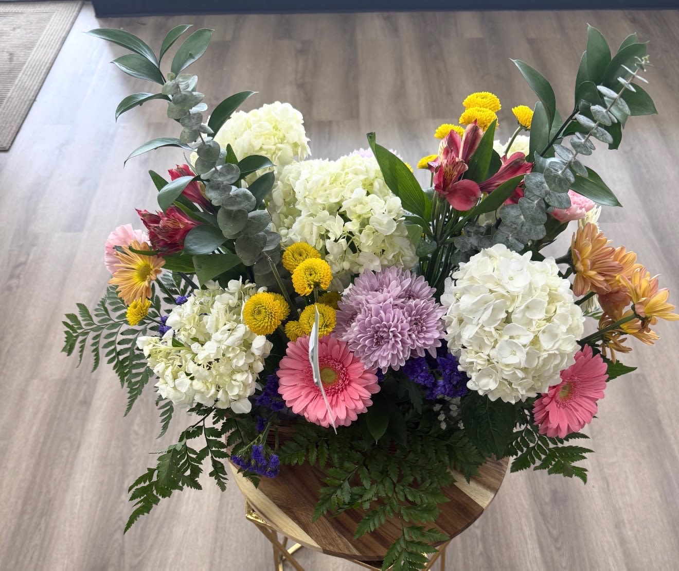 Sunshine Garden Arrangement - A vibrant garden-style arrangement overflowing with fresh white hydrangeas, pink gerbera daisies, soft chrysanthemums, yellow button poms, alstroemeria, statice, and lush greenery. Designed with a cheerful blend of colors and textures, this piece brings warmth, joy, and natural beauty to any space. Perfect for birthdays, celebrations, get-well wishes, or brightening someone’s day with a burst of spring-inspired charm.