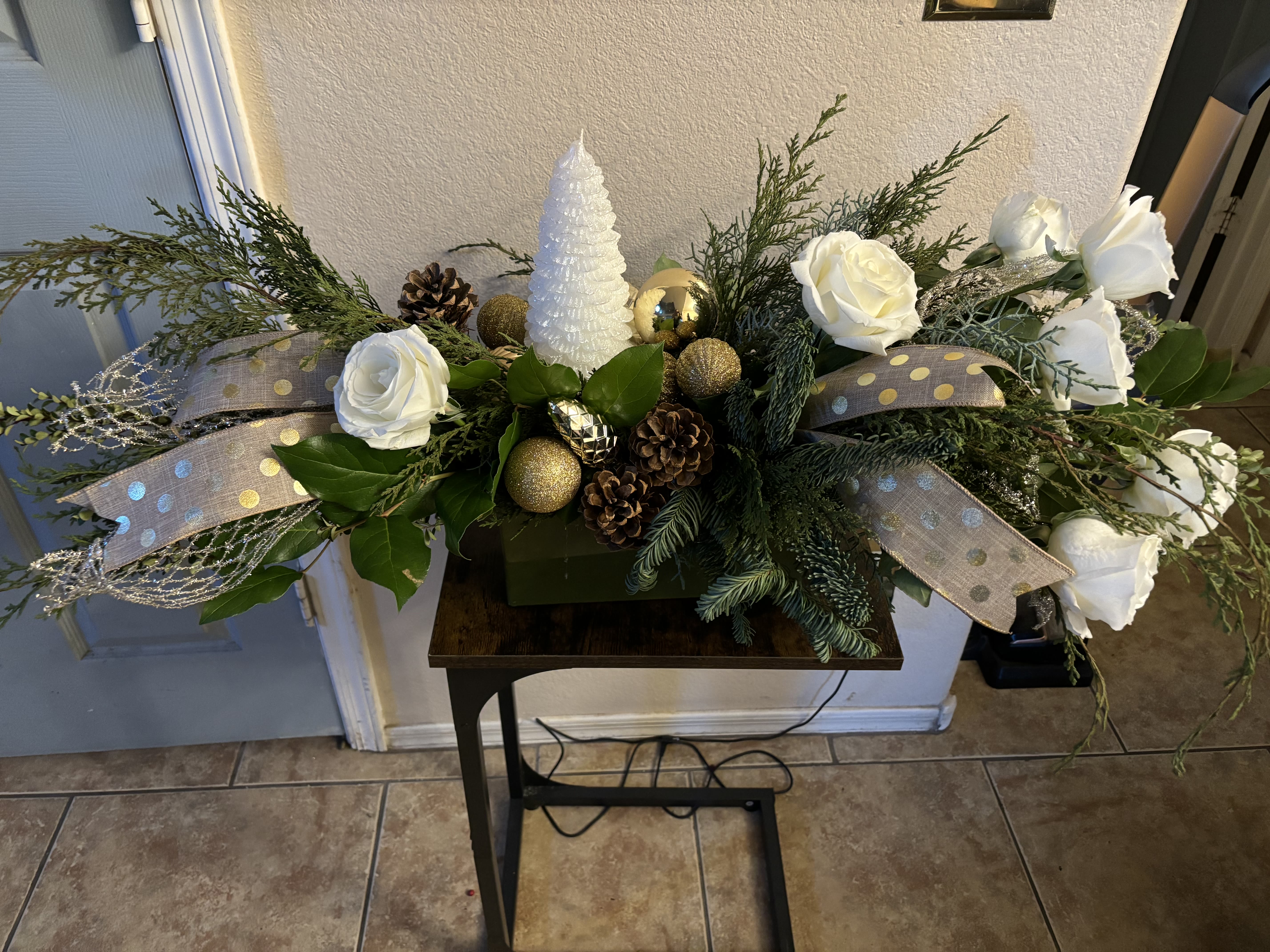 White christmas  - Long and low with white holiday tree candle ,  Includes lots of mixed greenery , pine cones , gold bulbs and ribbon and white roses.   Red roses can be added upon request.   Or upgrade and add  green cymbidium orchids 