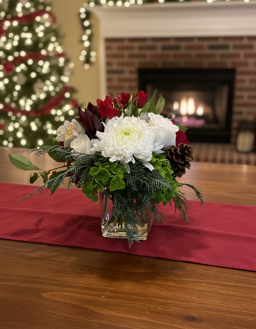 Christmas Mae's Garden - A timeless holiday arrangement designed to bring the warmth of Christmas indoors. Christmas Mae’s Garden features crisp white blooms nestled among rich seasonal greenery, accented with deep red florals, natural pinecones, and festive textures. Arranged in a clear glass cube, this piece feels both traditional and fresh—perfect for a dining table, mantel, or thoughtful holiday gift. Elegant, cozy, and full of seasonal charm, it’s a beautiful way to celebrate the spirit of Christmas.