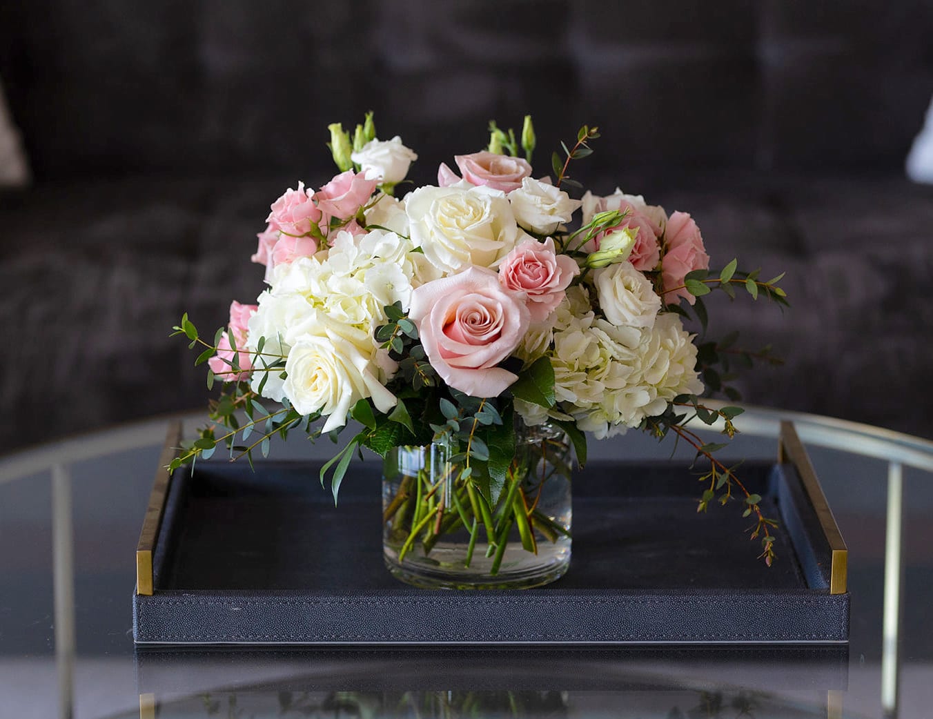 Blush Collection - Market Size  - Dreamy shades of pink, peach, and ivory—reminiscent of a vintage English garden—come together in our Blush Collection. This arrangement features peach "Shimmer" garden roses, soft pink Premium roses, white Lisianthus, and crisp white hydrangea, accented with Italian Ruscus and Eucalyptus greenery.  Our Market size arrangements feature fresh cut flowers in a clear glass vase. We created this size to send for birthdays, a pick-me-up, a thank you or to also work as a centerpiece for parties and events. These designs are made in a 5” clear glass cylinder vase.   Product Details: The market size arrangements are approximately 10” tall and 8” wide. The Premium size includes an additional 10 stems of flowers and greenery. 