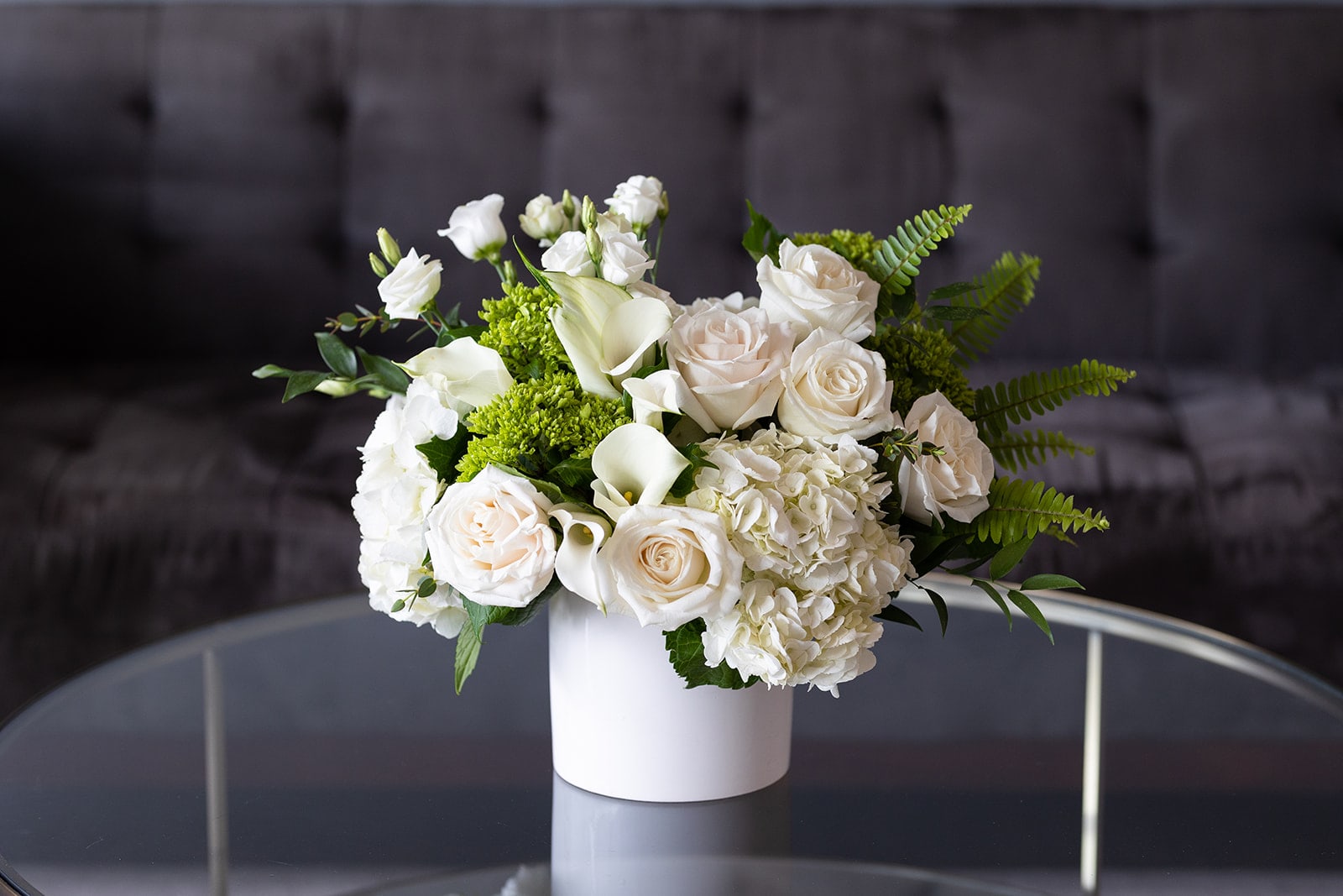 Comfort Collection - Signature Size  - Shades of white are proven to create a sense of calm, restfulness and harmony. Our Comfort Collection was designed to soothe the soul while lifting the spirit. Perfect for sending sympathy or healing. Also a lovely and sophisticated look for a private party. Includes hydrangea, calla lilies, garden roses, mini green hydrangea, Lisianthus and accents of fern.   Our J. Morris Signature designs are perfect for an anniversary, birthday, as a thank you, or as a larger centerpiece for a kitchen island or table. They are low enough to see over but are still full, grand and filled with blooms. Featured in a matte white 6” ceramic vase.   Dimensions: J. Morris Signature arrangements are 15” high and 12 inches wide. The DeLuxe version includes an additional 10 stems. 