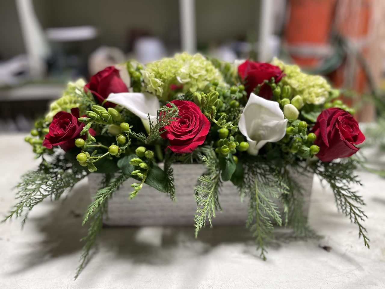 Centerpiece - Table centerpiece , arranged in rectangular 10 inches long -  Arranged with beautiful seasonal flowers - perfect to compliment those decorations or for a table centerpiece. Standing about 7-8 inches tall from table and about 15 inches overall - with red roses / white calla's / Mini green hydrangea /  seasonal greens. 