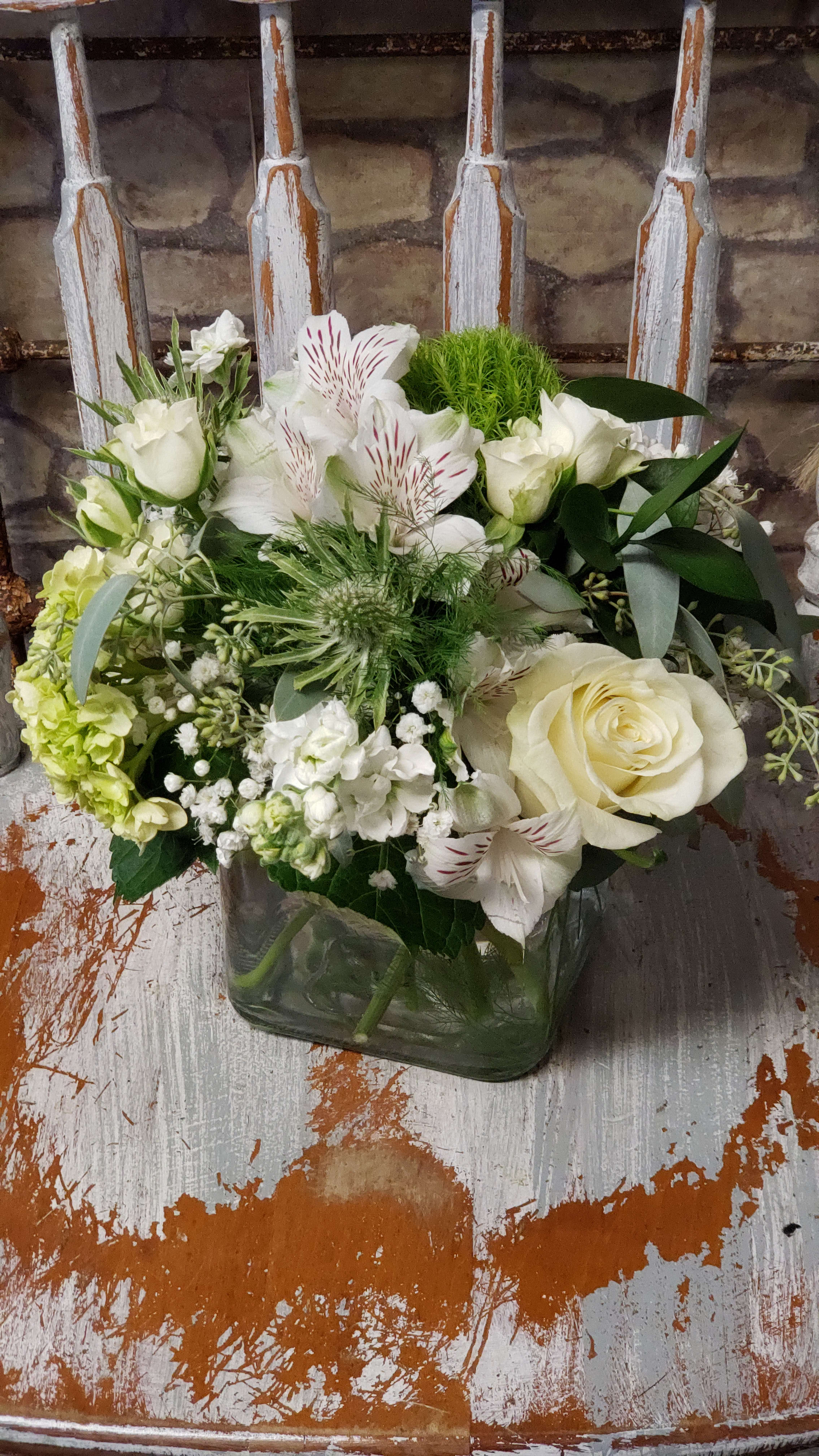 Peaceful Blooms - ALL WHITE-LIMITED Soft statement of color...white, cream &amp; greens. Blue or green Thistle when available. A variety of flower choices will be selected based on market fresh inventory at time of order &amp; delivery. Photo sample for size 4x4 cube &amp; style.  Glass cube in Pave' style, standard is in 4x4 cube. Deluxe 4.75 x 4.75 cube.