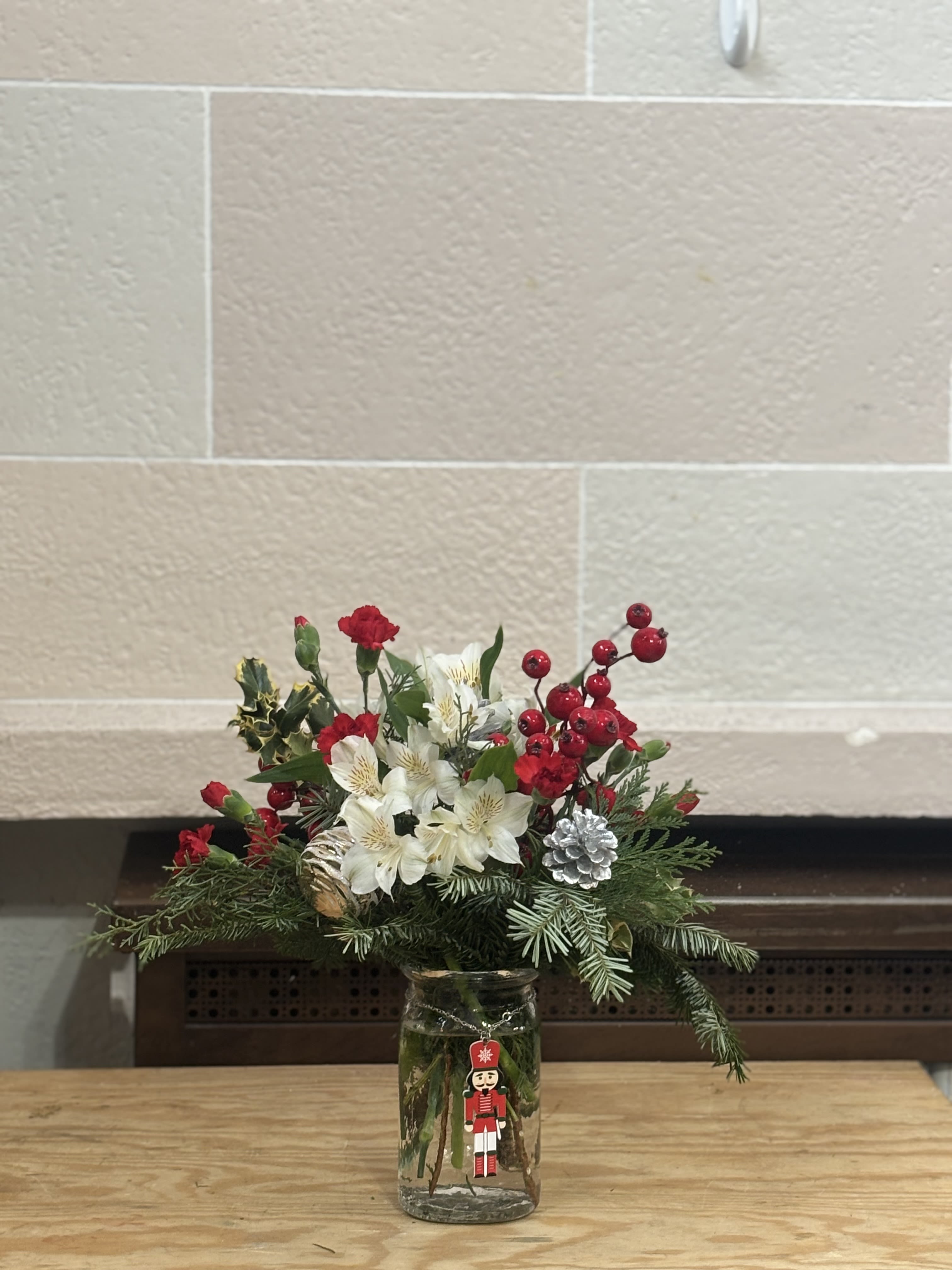 Medium Nutcracker Vase  - A medium jar style nutcracker vase filled with Christmas greens, carnations, alstroemeria, and artificial berries. 