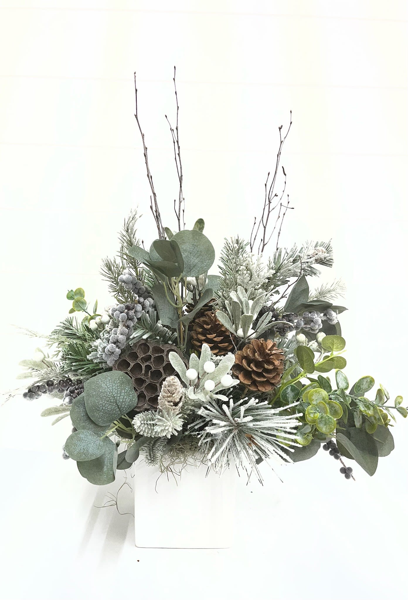 Frosted Winter Evergreens Faux Flowers - This artisan faux floral arrangement captures the essence of winter with beautifully textured pine cones, snowy white berries, and premium winter greens arranged in soft, natural layers. Lightly dusted with faux snow for a freshly frosted finish, it offers an elegant, maintenance-free display for your holiday home or winter events.