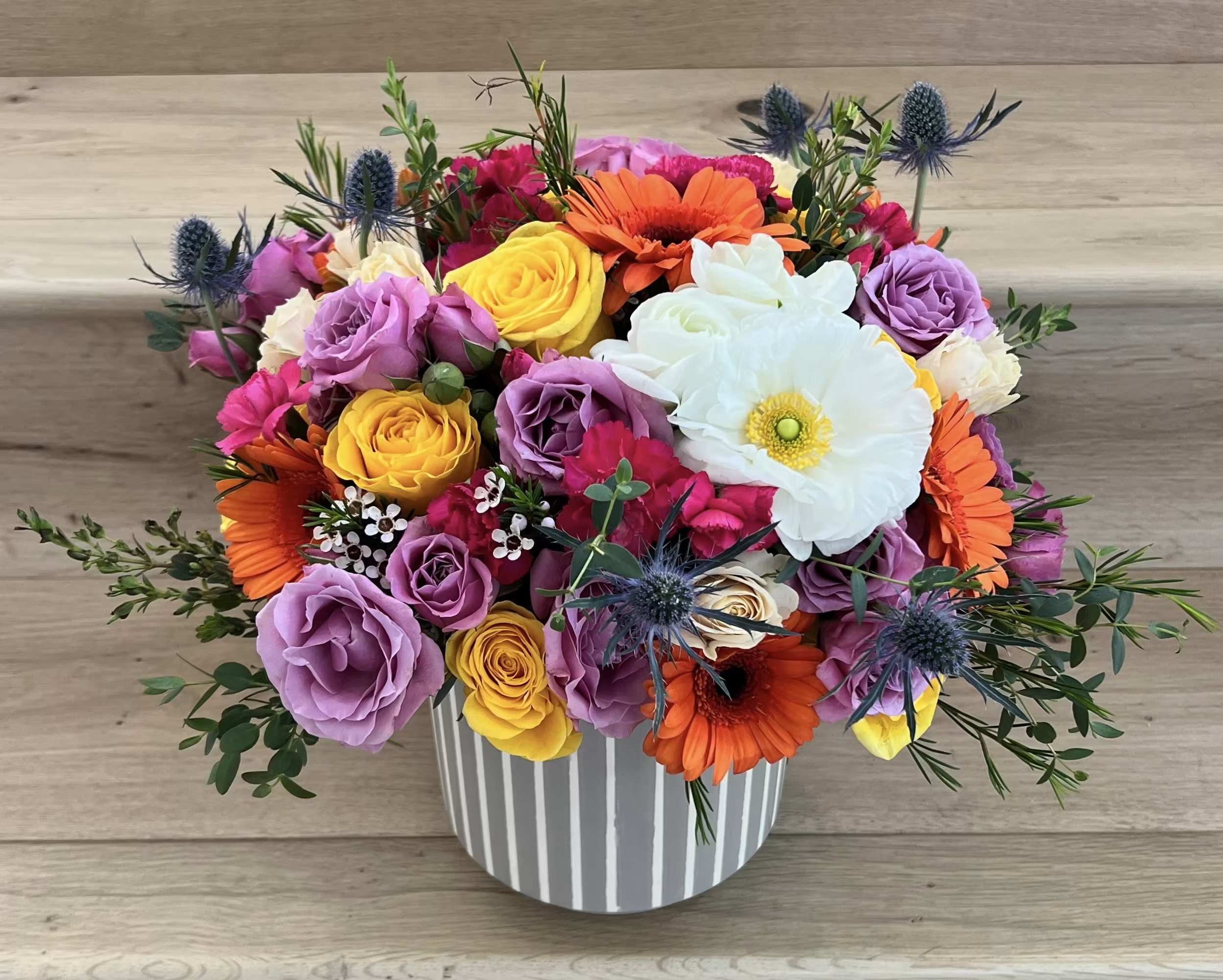 Colorful bouquet of roses, gerbera daisies, and a white anemone in a striped vase
