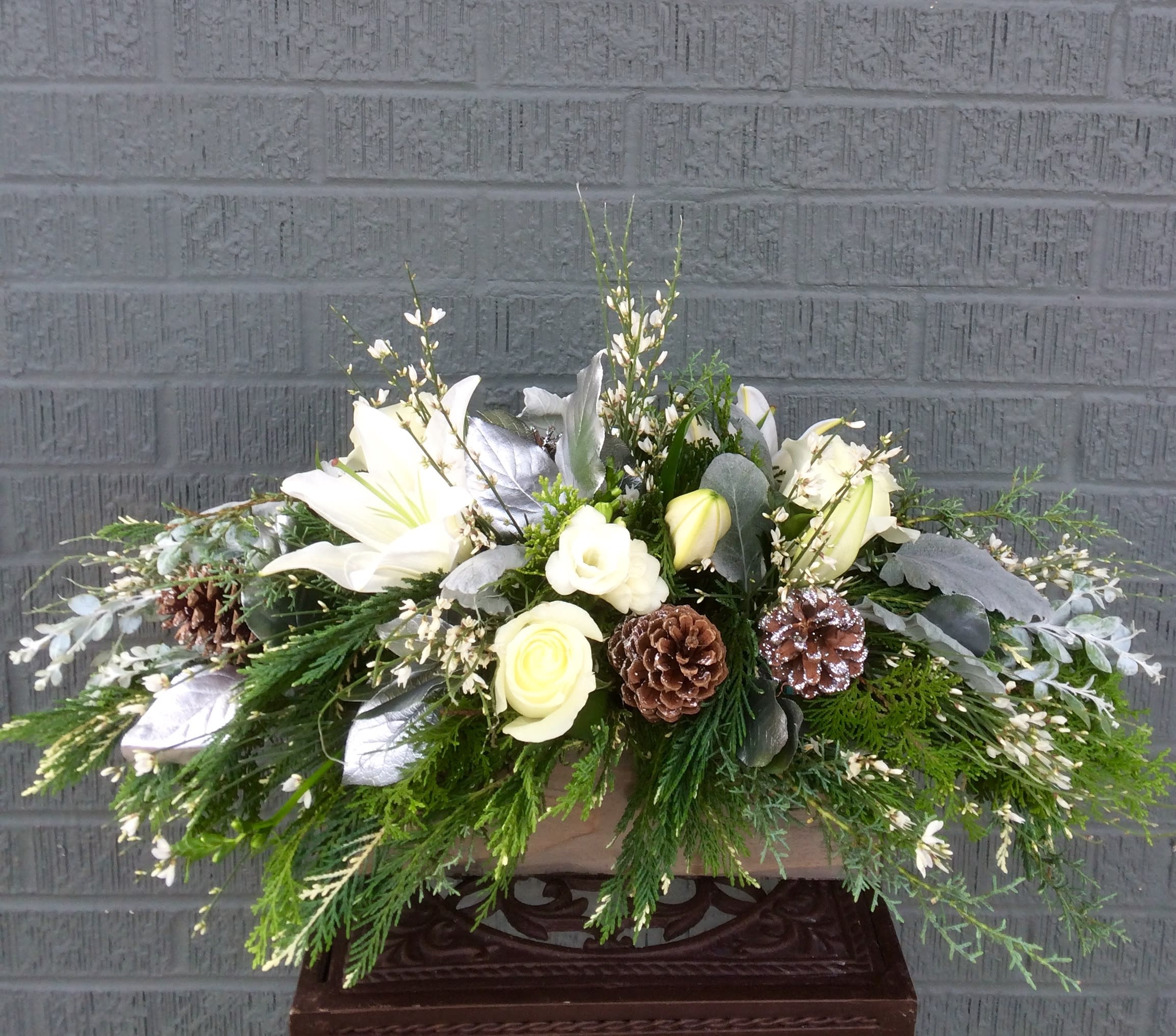 Wintery Wonderland Centerpiece - Beautiful oblong centerpiece created in a wooden box and filled with oriental lilies, white roses, silvered magnolia leaves, and pine cones with a base of specialty Christmas Greens. 25" long x 10" high