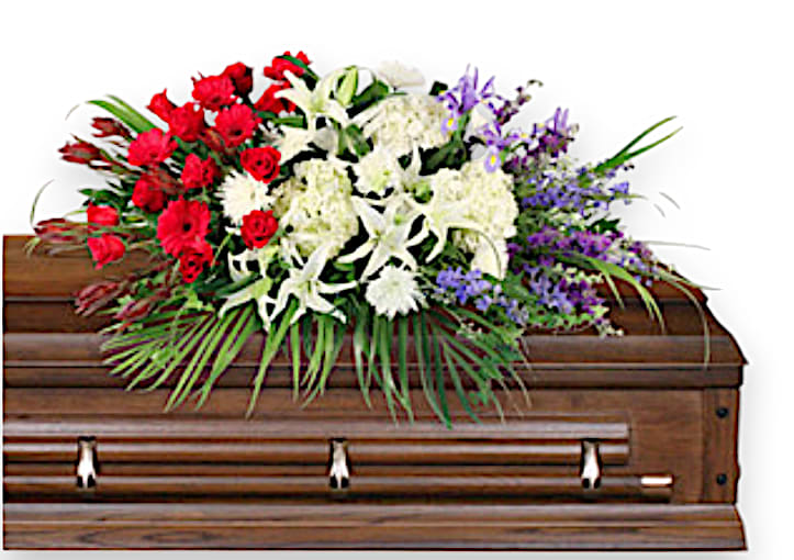 Brave Soldier Casket Spray - This striking sympathy arrangement is a breathtaking homage to a life well-lived, blending vibrant colors and textures to convey both sorrow and remembrance. At the heart of the design, ten luxurious red roses symbolize deep love and respect, while five radiant red gerberas add a cheerful touch of warmth. Surrounding these are three elegant white lilies and three pristine white hydrangeas, bringing a sense of purity and peace to the composition. The arrangement is artfully accented with six delicate white spider mums that enhance its soft aesthetic, alongside seven stems of purple larkspur and five regal purple irises, which introduce richness and complexity. Completing this harmonious ensemble are seven stems of striking blue delphinium, evoking a calming presence. This arrangement is framed by lush foliage, including teepee, ivy, salal, and ruscus, creating a verdant backdrop that encapsulates the beauty of cherished memories, making it a meaningful tribute during times of loss.