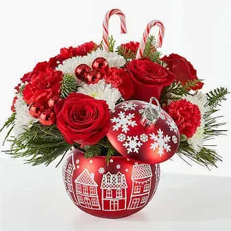 FTD Cheer in the Air Ornament Bouquet - A delightful village inspired ornament with bright, festive holiday colors!  Carnations, roses, white chrysanthemums and holiday greens will put fill you with holiday cheer!