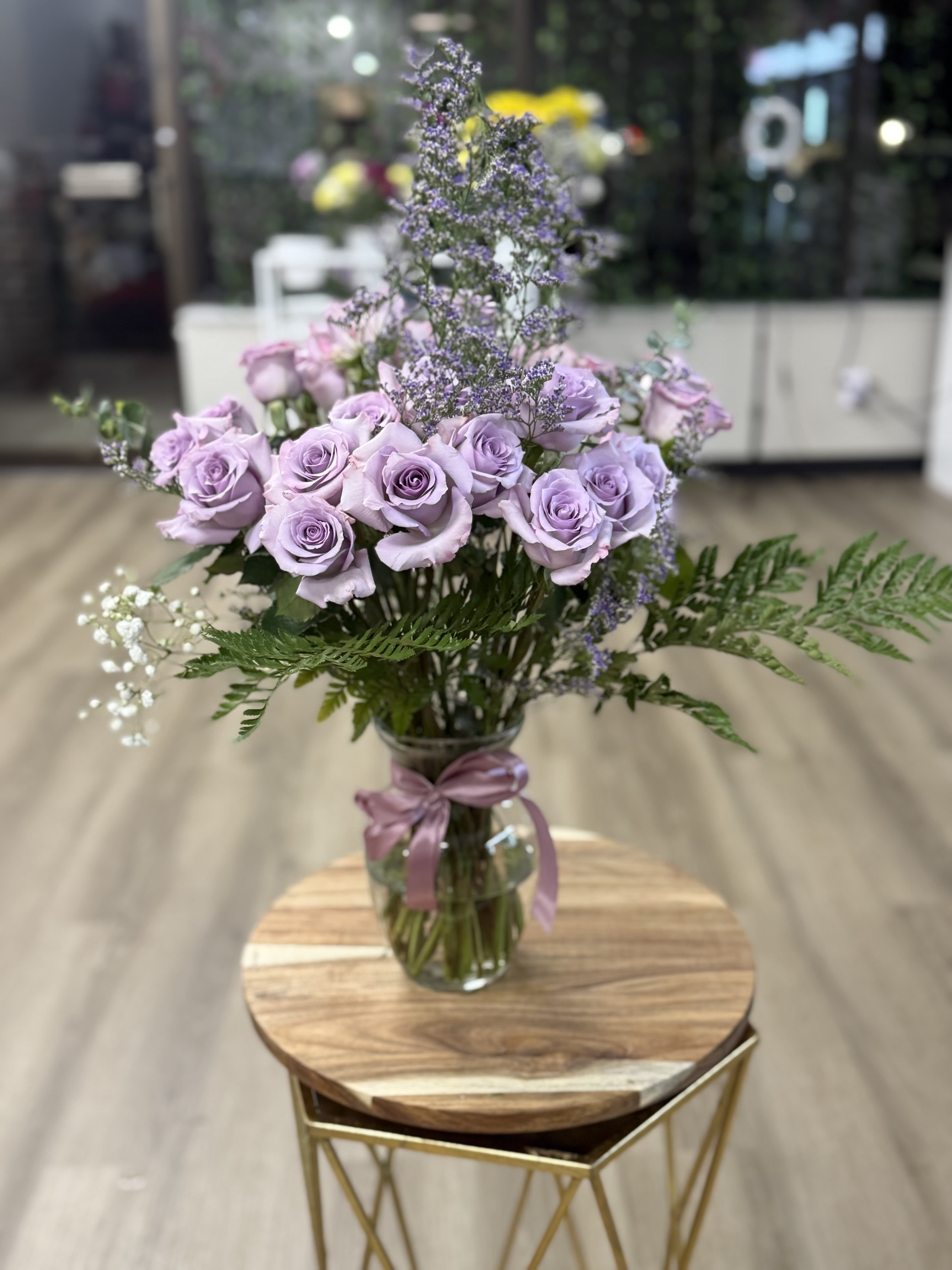 Lavender Elegance Vase 24 roses - A graceful and romantic display featuring lavender roses arranged with delicate baby’s breath, limonium, and fresh greenery. Presented in a clear vase and finished with a lavender ribbon, this arrangement offers a soft, timeless beauty perfect for anniversaries, birthdays, sympathy, or expressing heartfelt sentiments with elegance.