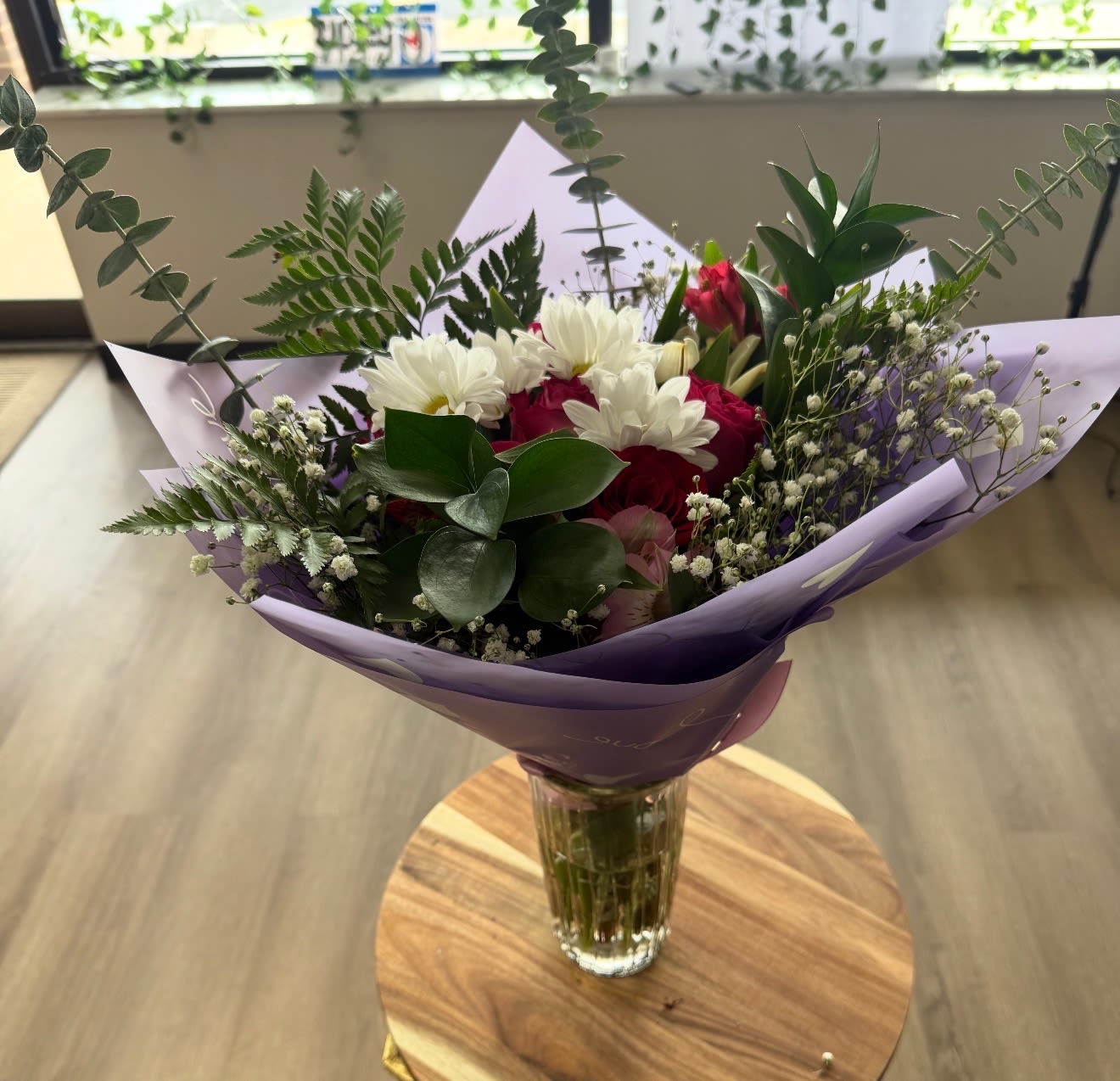 Lavender Love Bouquet -  This beautifully wrapped bouquet features a fresh mix of red roses, white daisies, alstroemeria, eucalyptus, baby’s breath, and lush greenery, all arranged in elegant lavender wrapping. Soft, romantic, and full of charm, it’s the perfect gift for birthdays, anniversaries, thank-you gestures, or simply brightening someone’s day with a touch of beauty.