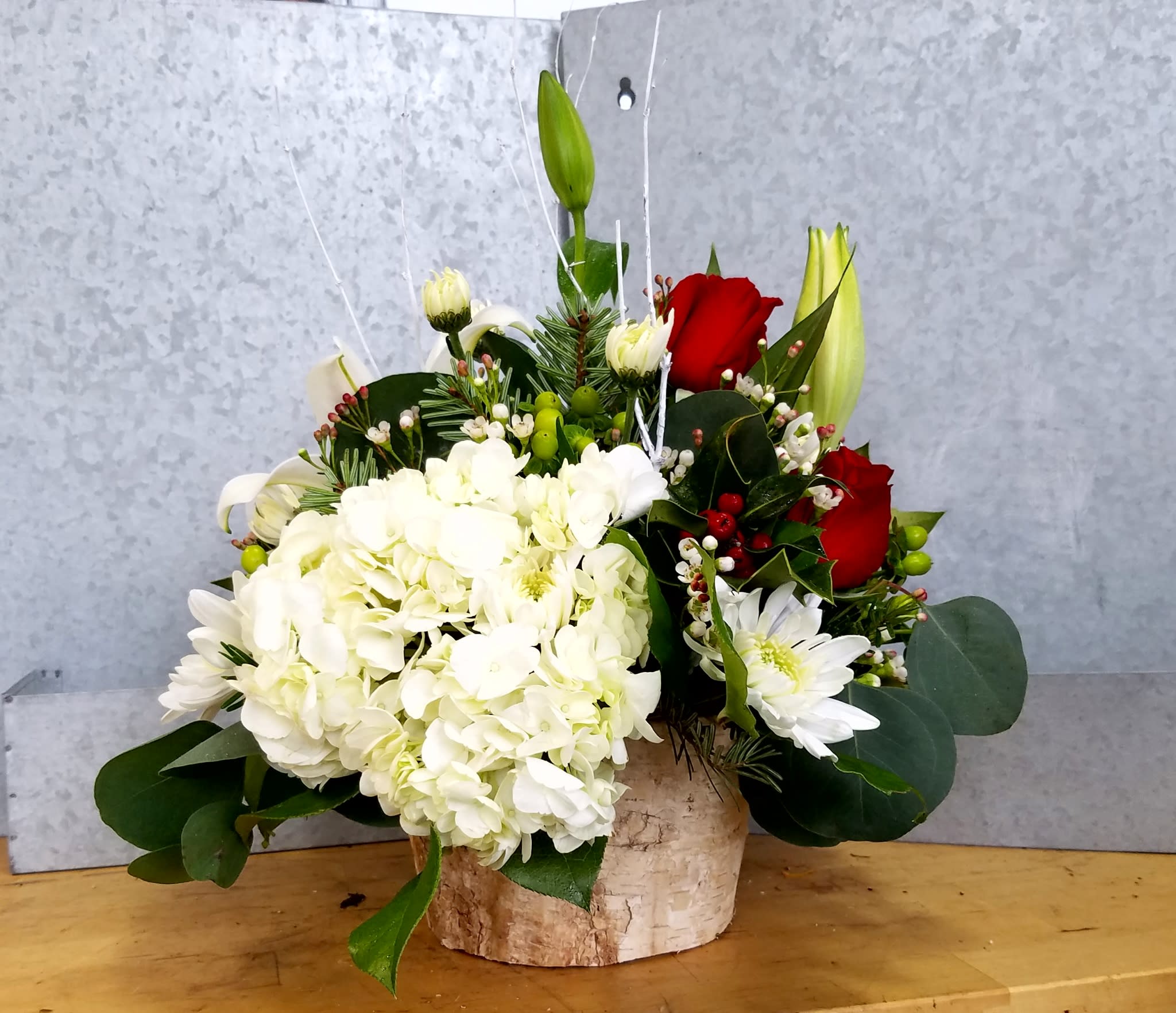 Winter Wonder - Here's a fresh take on seasonal Christmas colors.  This elegant arrangement comes in a birch-wrapped container, enhancing the natural look.  Eucalyptus and Holly greens set the platform for a lush hydrangea, elegant white lilies, and classic red roses.