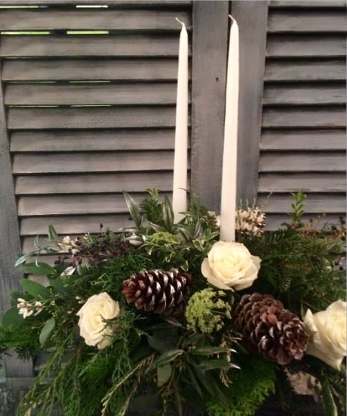 Snowy Pines Centerpiece  - Elegant oblong centerpiece featuring white roses with silvery foliage, specialty evergreens, silver splashed pine cones, and seeded euc. with white candles.