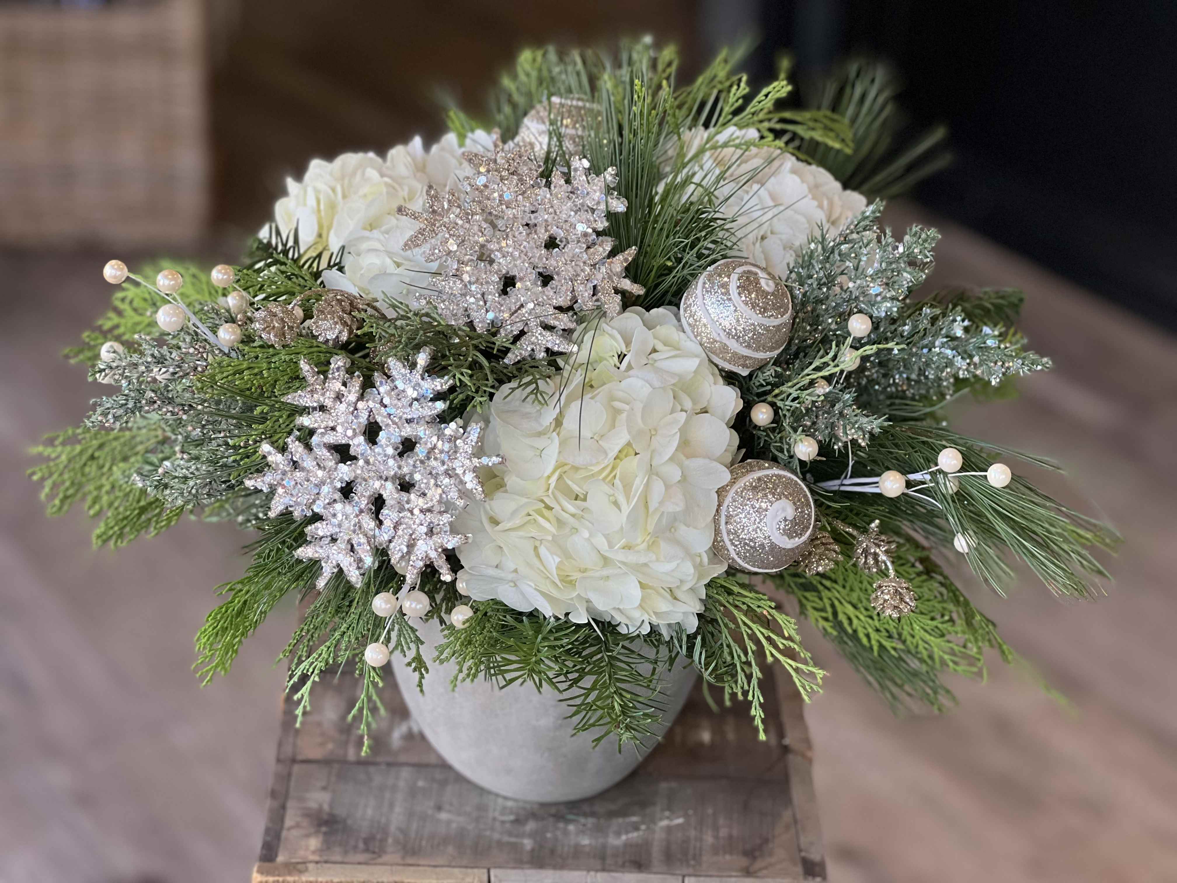 Champagne Snowfall - Lush white hydrangea is nestled among fragrant holiday greens and accented with champagne-toned ornaments and delicate winter details. Elegant, serene, and timeless — perfect for formal entertaining or quiet holiday gatherings.
