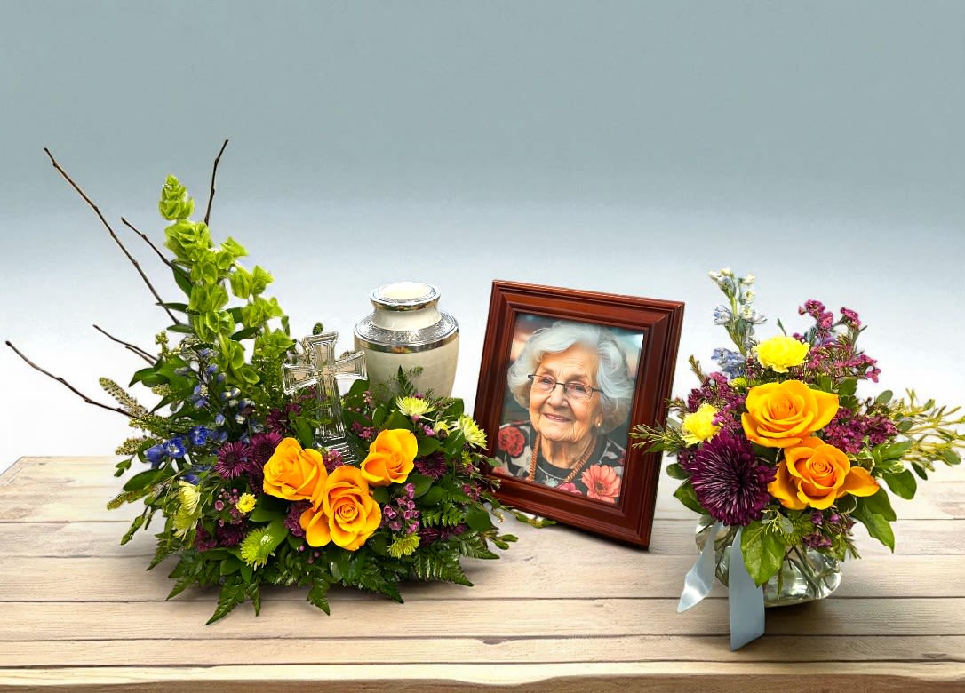 Heavenly Garden Collection - This heartfelt sympathy arrangement features a beautifully coordinated display designed to honor and remember a loved one. The arrangement includes a lush, vibrant bouquet of orange-yellow roses complemented by an array of colorful seasonal blooms and greenery, creating a warm and comforting presence. Paired with a matching vase arrangement, both pieces are thoughtfully arranged to surround an urn and a cherished photograph of the deceased. Together, these floral tributes offer a serene and dignified tribute, serving as a lasting symbol of love, remembrance, and peace during a time of mourning.  Urn and Photo not included.  Urn riser included.