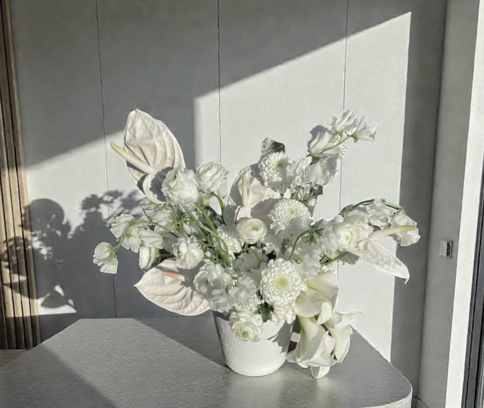Snowfall - Soft, sculptural, and quietly luxurious, Snowfall is a modern winter-white floral arrangement designed to feel timeless and refined.  This piece features a curated blend of premium white blooms layered with elegant textures and movement, finished in a ceramic vessel that complements its clean, elevated aesthetic.  Custom anthuriums add a luminous touch—catching the light beautifully and giving this arrangement its signature presence.   Designed with intention, Snowfall is effortless yet impactful, making it perfect for winter gifting, luxury interiors, corporate settings, and refined holiday moments.  Whether styled in a modern home, office, hotel lobby, or executive space, this arrangement embodies understated elegance and contemporary floral design.  Please note: Each arrangement is created with seasonal availability in mind. While the overall look and feel will remain consistent, flower varieties may vary slightly to ensure the highest quality and freshness.