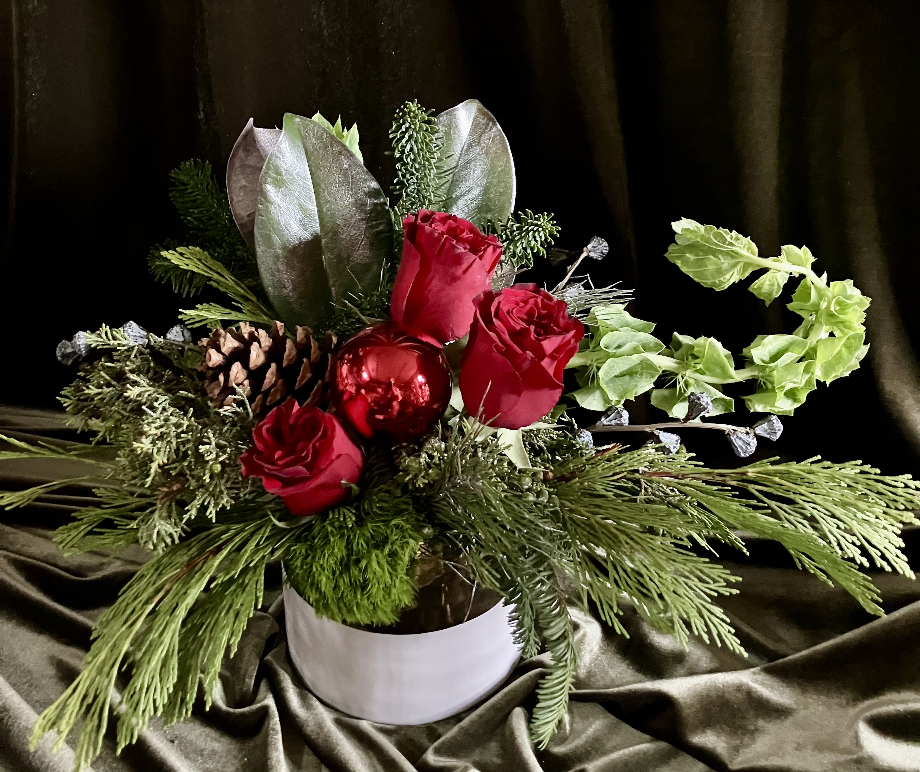 Just For Fun  - Fresh evergreens, silver magnolia leaves and pine, with red roses, bell of Ireland eucalyptus pods and a large pine cone and ornament in the center in a white and gold container 